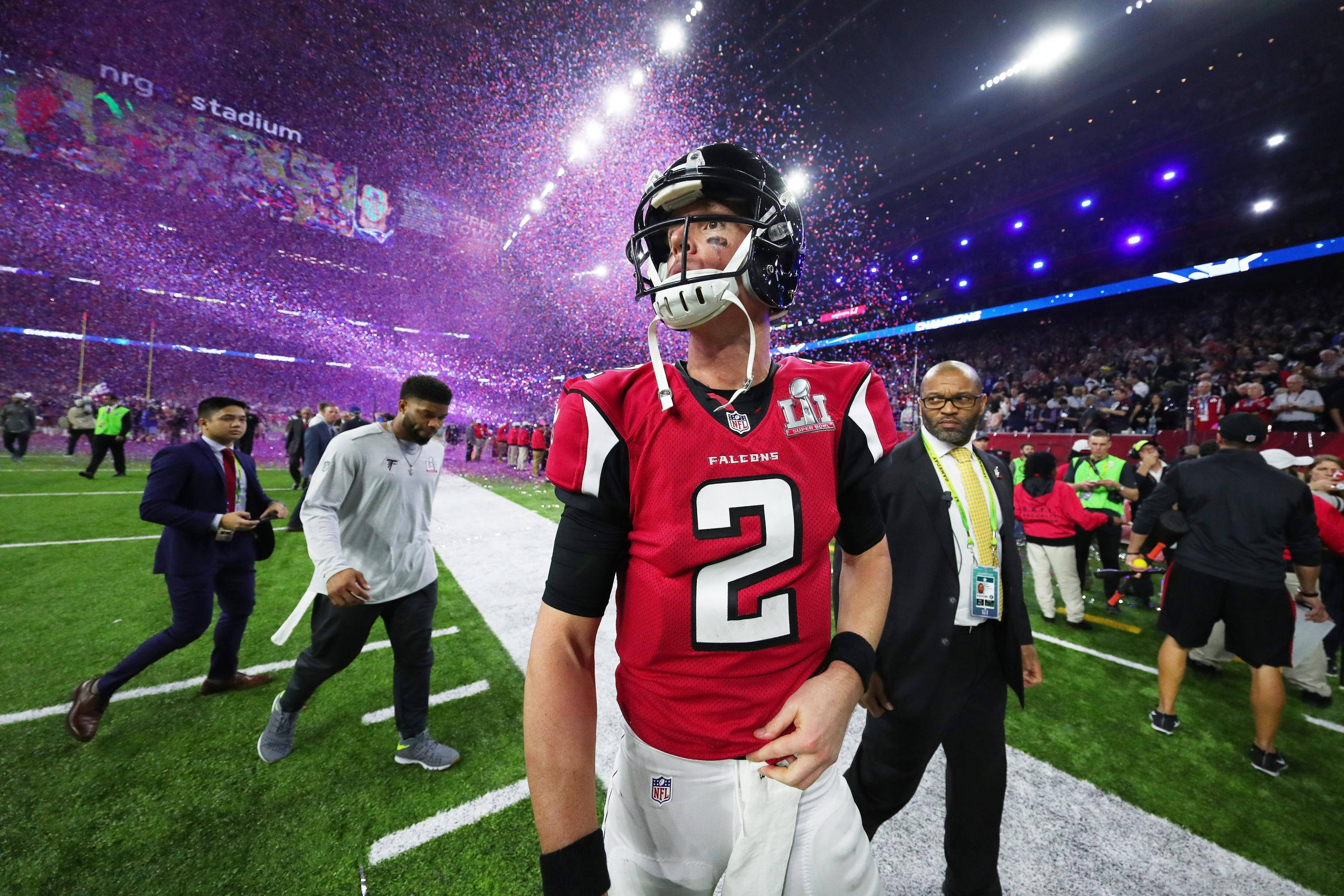 Matt Ryan 桌布 壁紙 — 一名身穿紅色Falcons球衣的足球員在體育場燈光下，紫色紙屑如雨般飄落時步出球場。