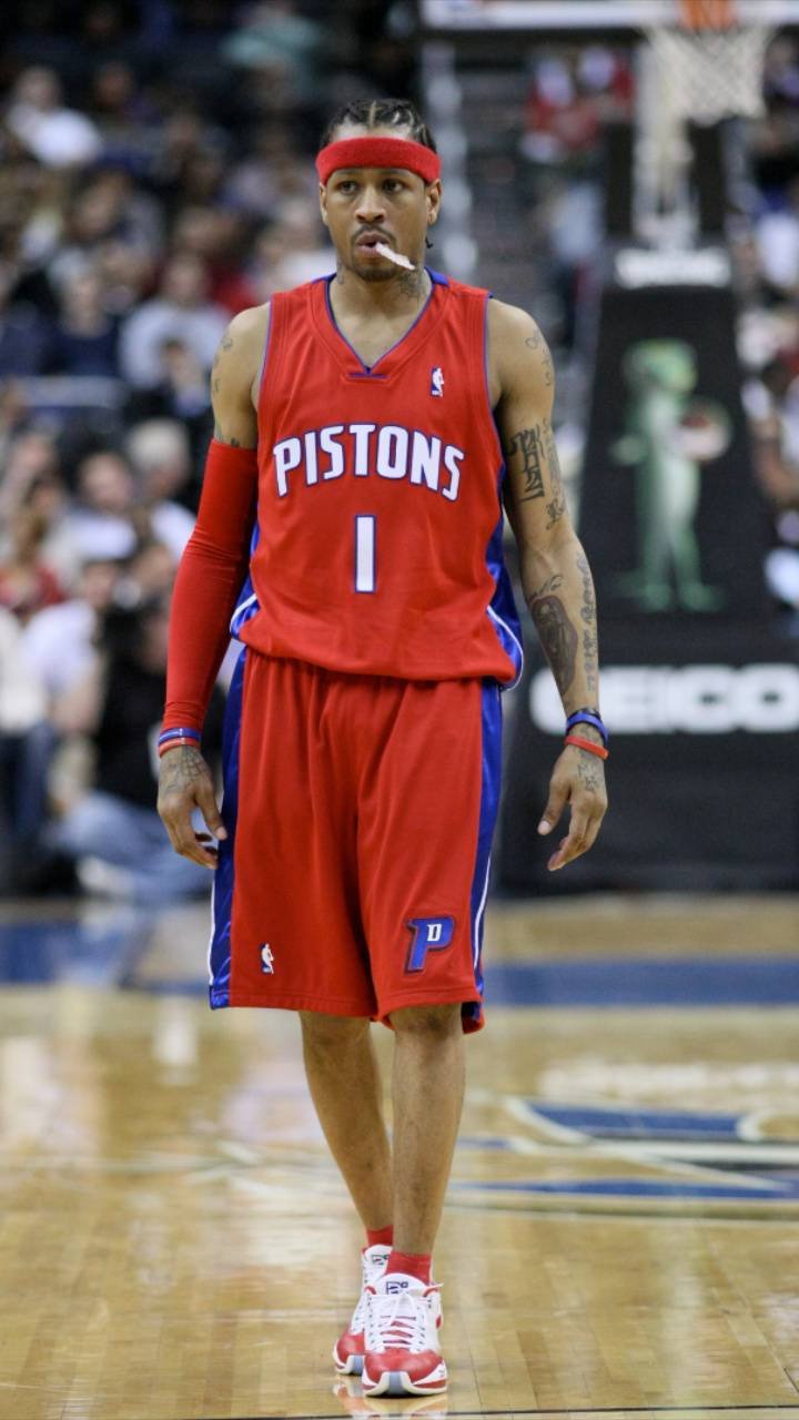 NBA iPhone 桌布 壁紙 — 一名身穿紅色Pistons球衣的籃球運動員在木地板上行走，手臂上的紋身清晰可見。