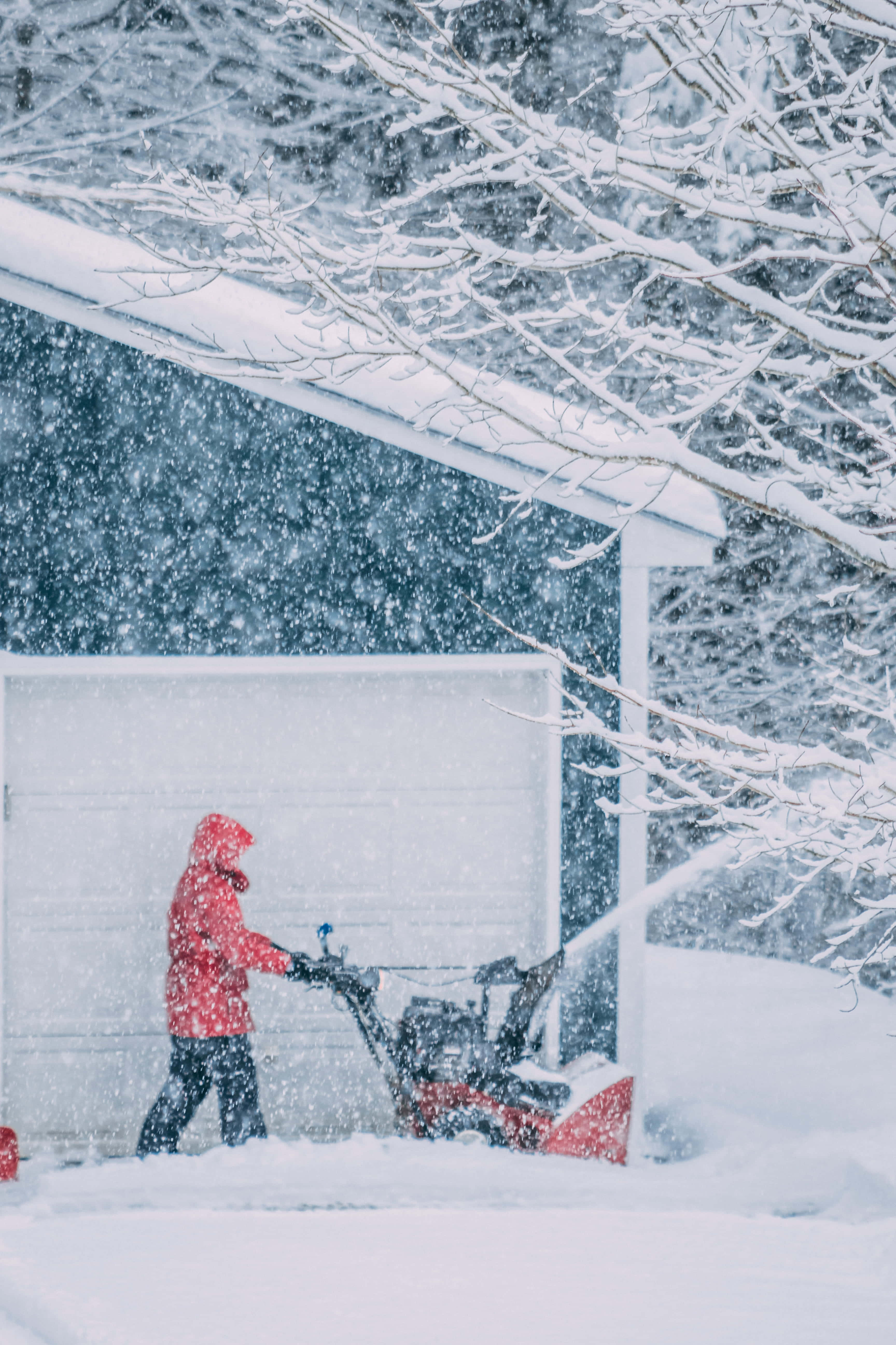 Snowplow 桌布 壁紙 — 一名身穿紅色外套的人在大雪中從車庫旁的車道剷雪。