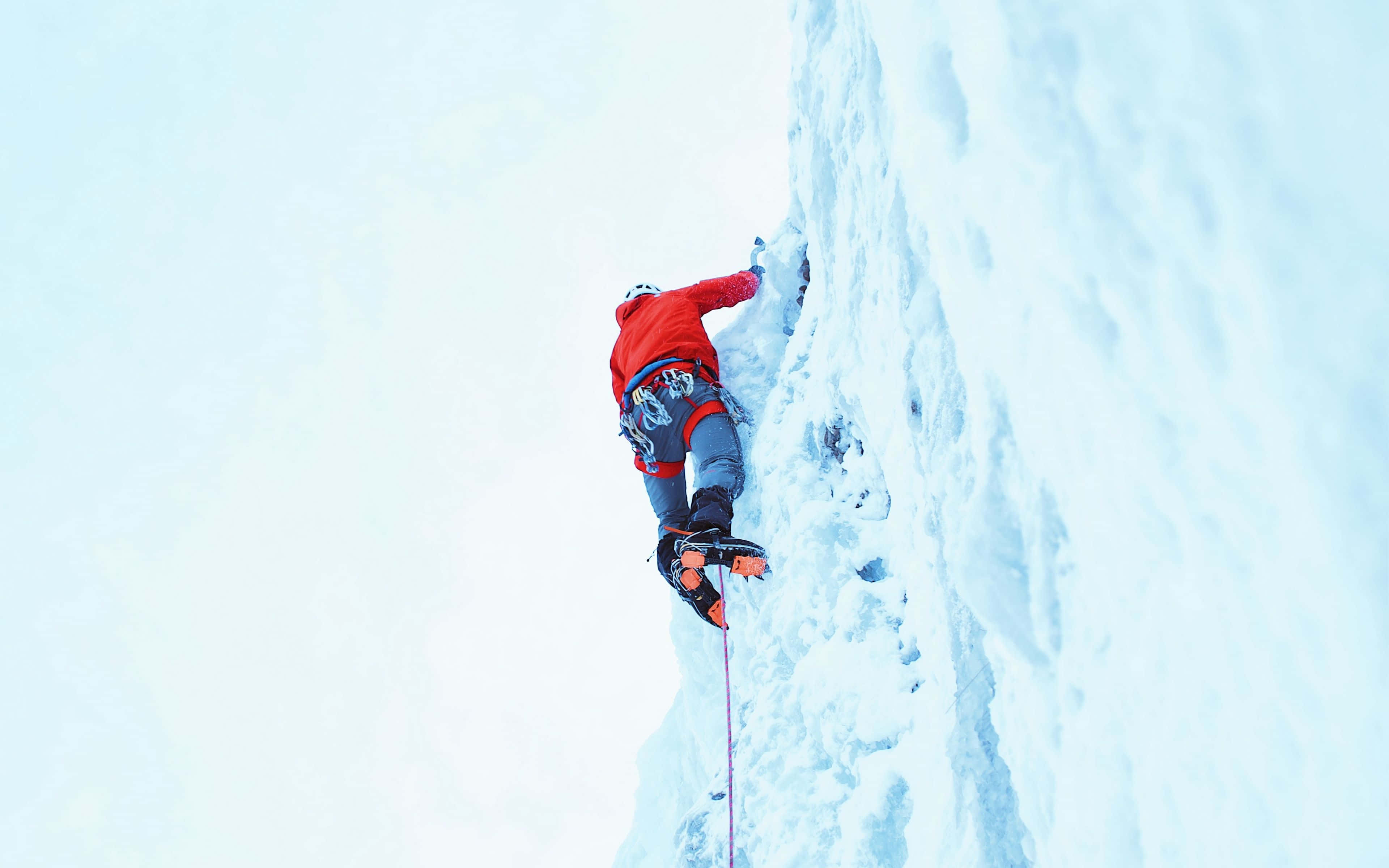 Ice Climbing 桌布 壁紙 — 一名身穿紅色外套的攀岩者，正用冰爪和冰斧攀爬陡峭的積雪冰壁。