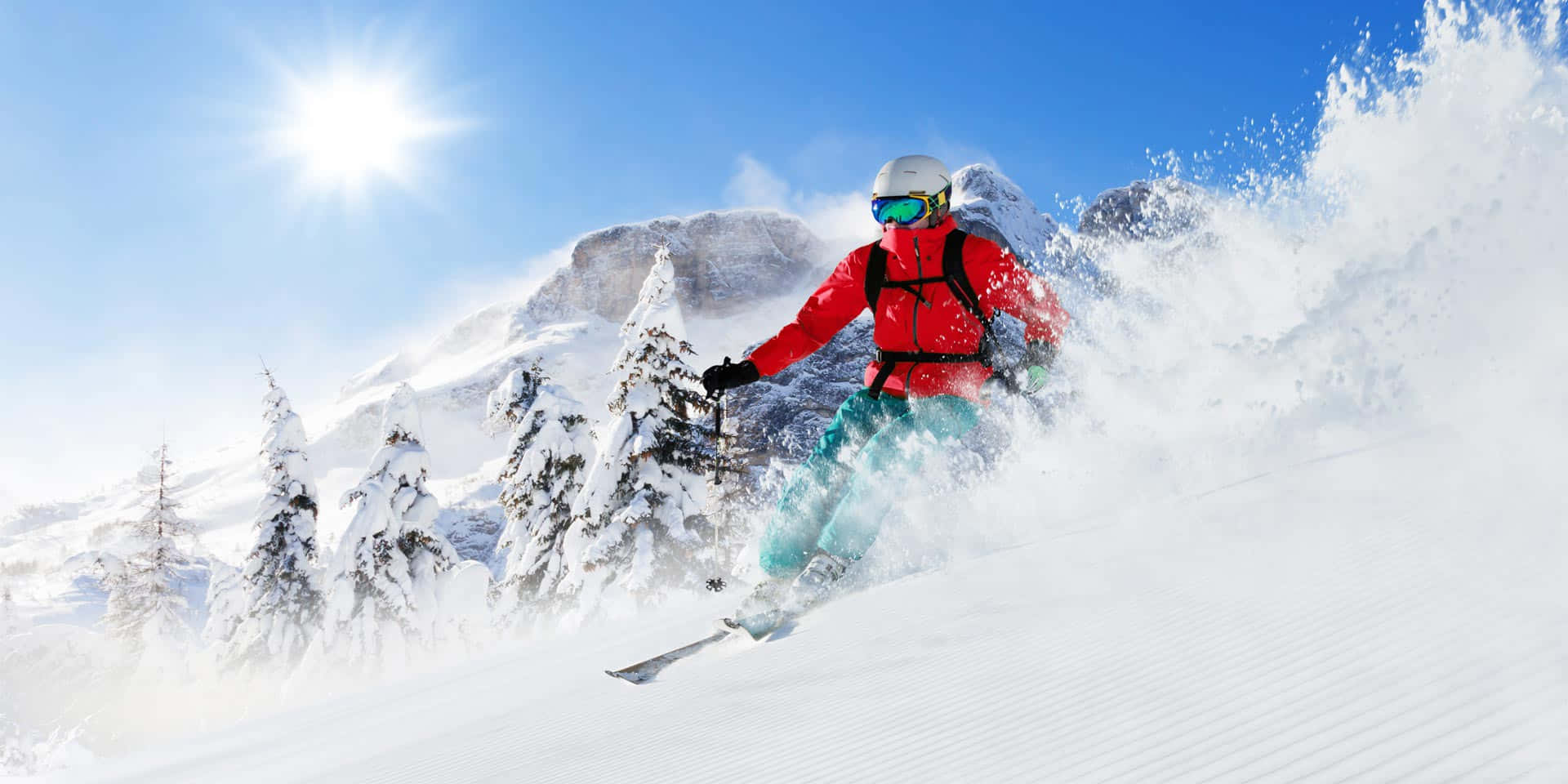 Winter Sports 桌布 壁紙 — 一名身穿紅色外套的滑雪者在陽光明媚的日子裡，在白雪覆蓋的松樹和岩石山峰背景下，穿過新鮮的粉雪。