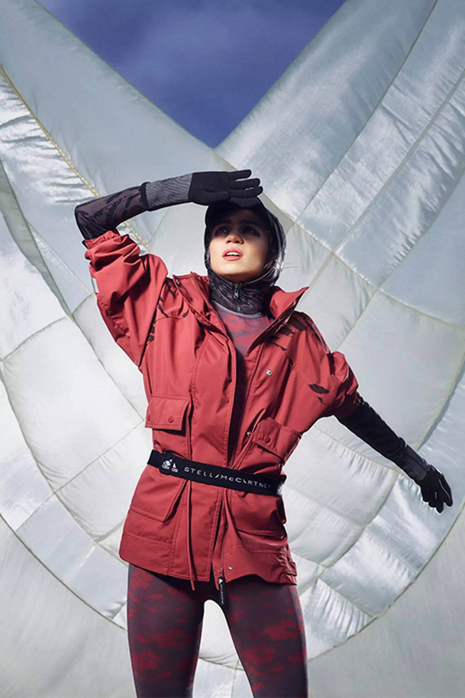 Stella McCartney x Adidas 壁紙 — 一名身穿紅色戶外外套和圖案緊身褲的女子站在白色熱氣球內部，背景是藍天。