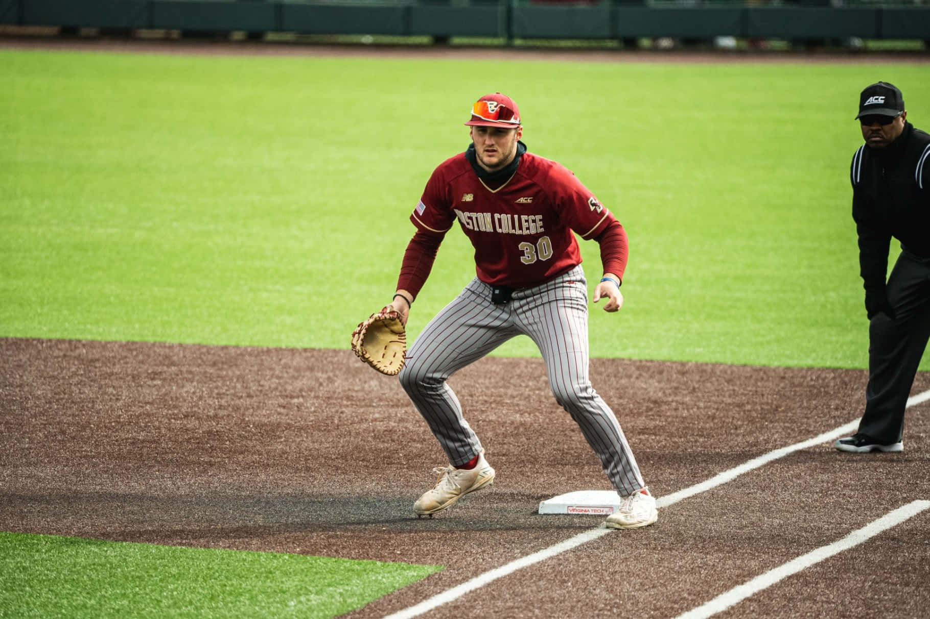 College Baseball 桌布 壁紙 — 一名身穿紅色波士頓學院球衣的棒球手在日間比賽中蹲在壘包附近準備防守。
