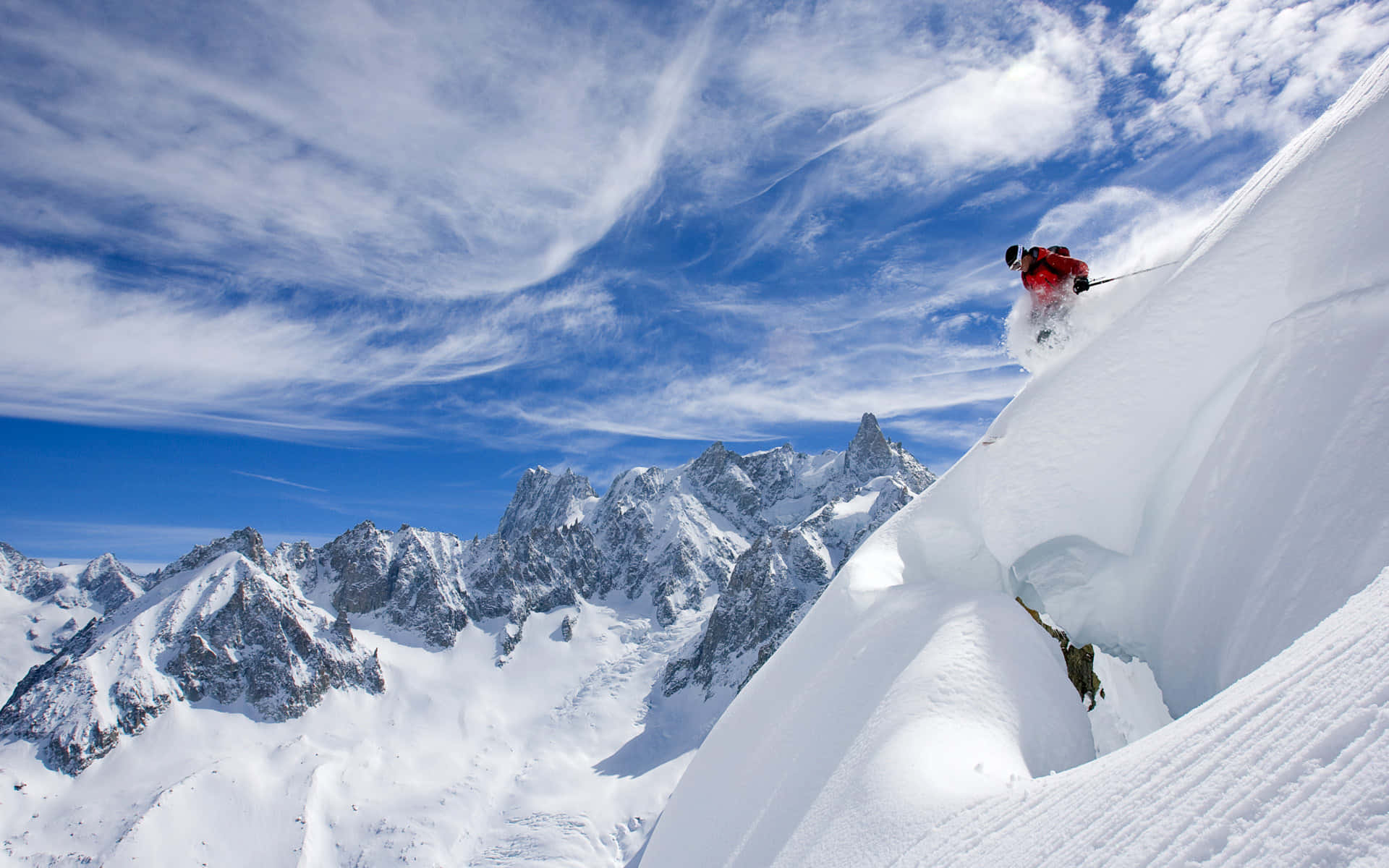 Skiing 桌布 壁紙 — 一名身穿紅色滑雪服的滑雪者在陡峭的山坡上，於薄雲點綴的湛藍天空下，在深厚的粉雪中劃過。