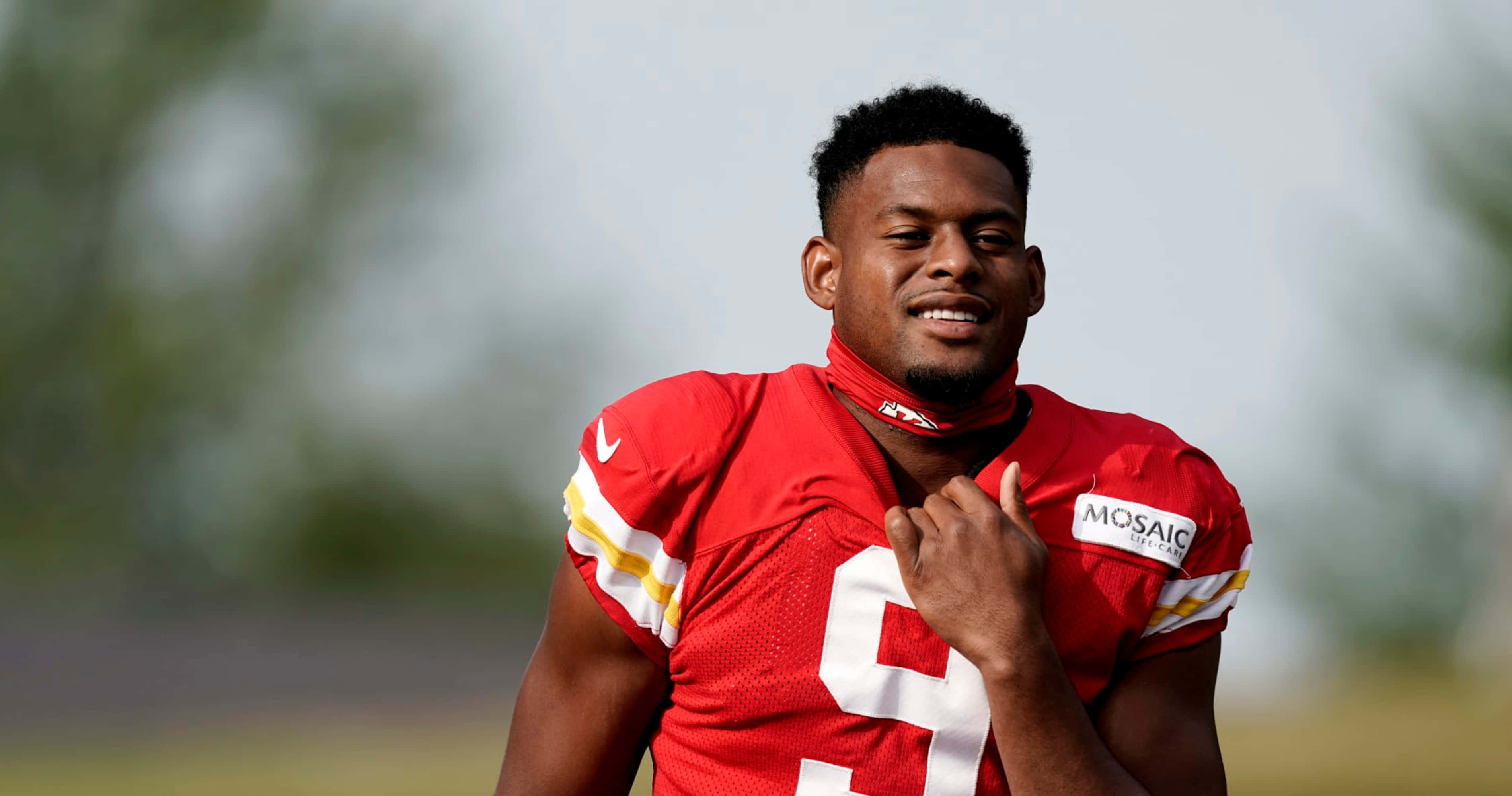 Juju Smith Schuster 桌布 壁紙 — 一名身穿紅色球衣、背號9的足球運動員在戶外微笑著調整衣領。
