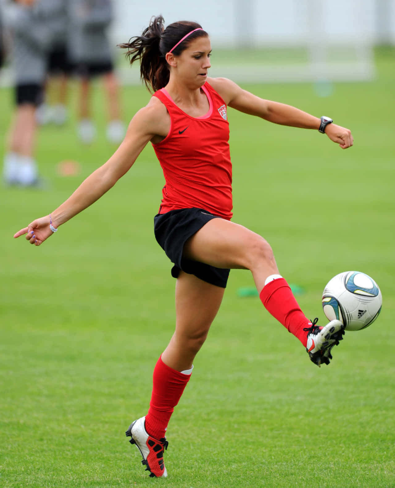 Alex Morgan 桌布 壁紙 — 一名身穿紅色球衣的女足球員在白天訓練時，在充滿活力的綠色場地上踢一個白色足球。