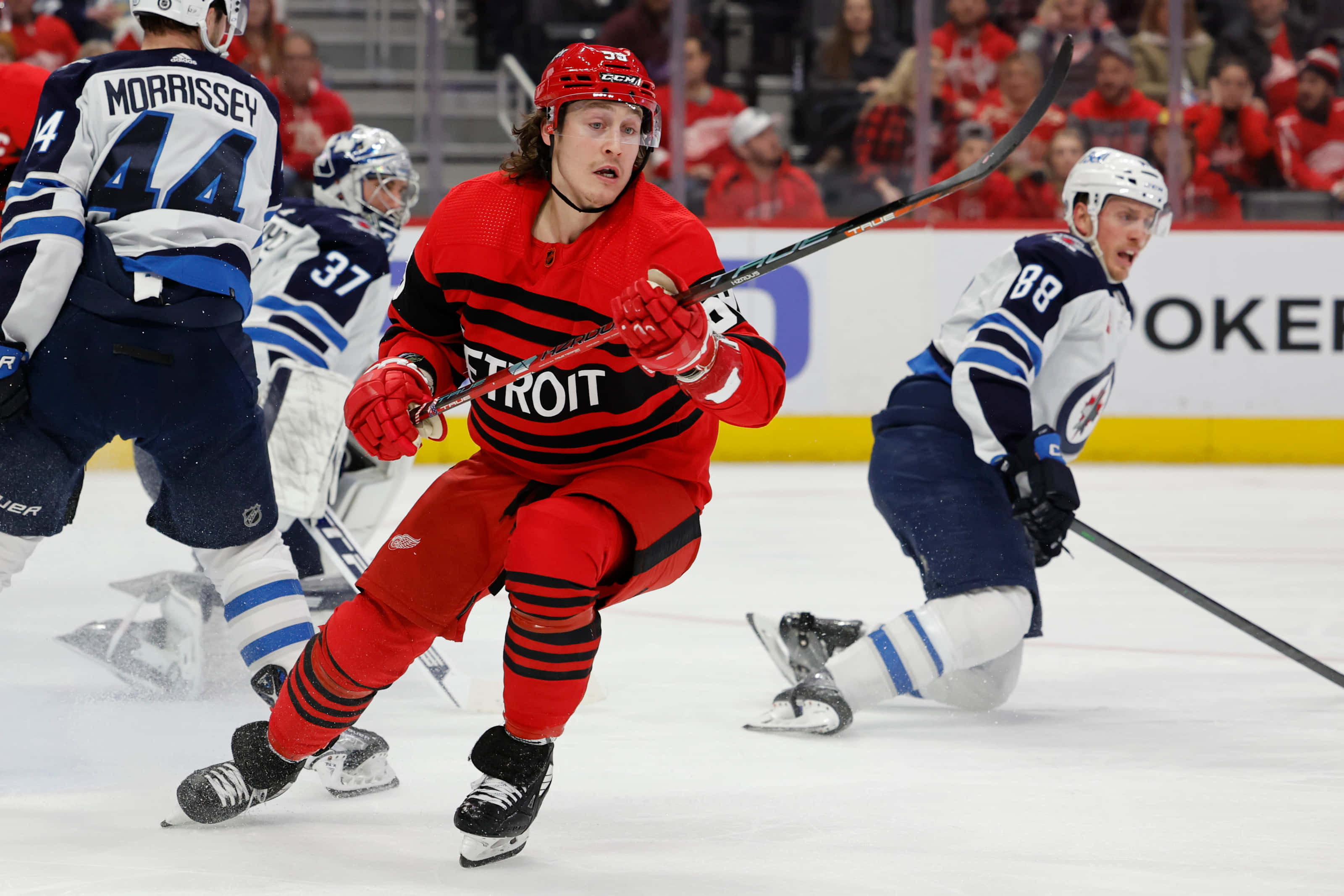 Tyler Bertuzzi 桌布 壁紙 — 一名身穿紅色球衣的底特律紅翼冰球球員在冰上與溫尼伯噴射機隊球員爭奪冰球。