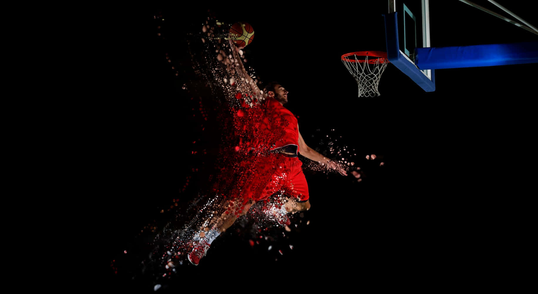 Cool Basketball 桌布 壁紙 — 一名身穿紅色球衣的籃球運動員在半空中扣籃時爆炸成粒子，背景為黑色。