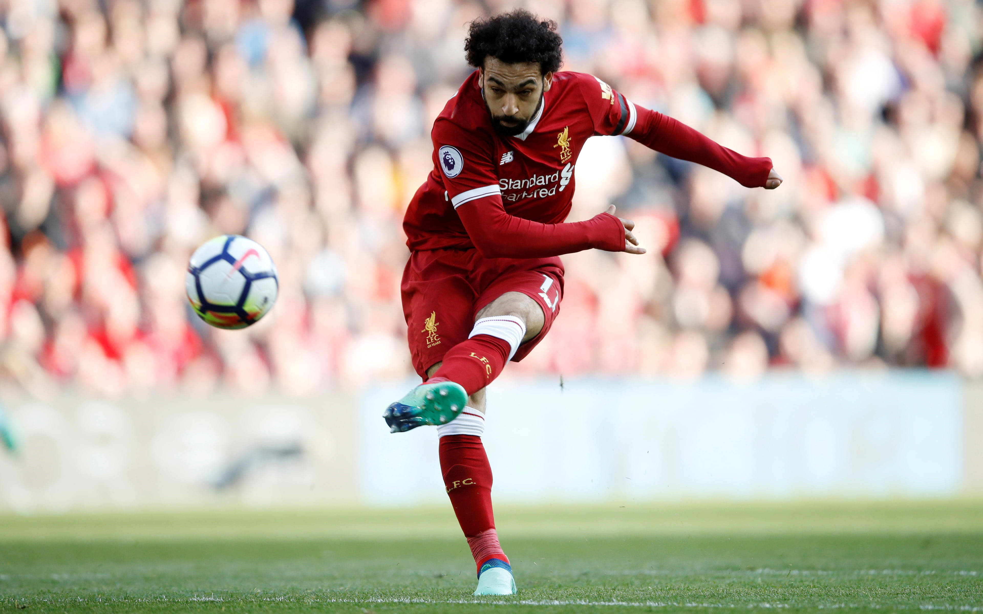 Liverpool Fc 桌布 壁紙 — 一名身穿紅色球衣的足球員在綠色球場上凌空踢足球，背景是模糊的人群。
