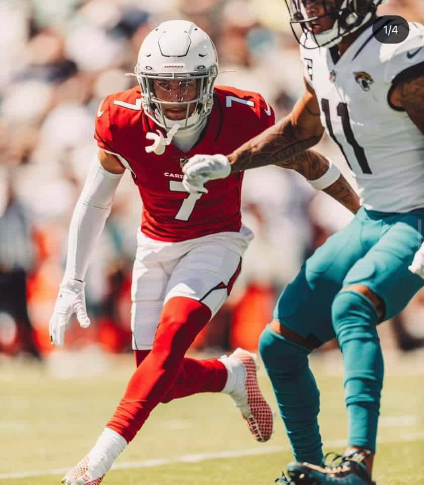 Byron Murphy 桌布 壁紙 — 一名身穿紅色球衣的足球員在陽光明媚的球場上，衝過一名身穿藍綠色球衣的防守球員。