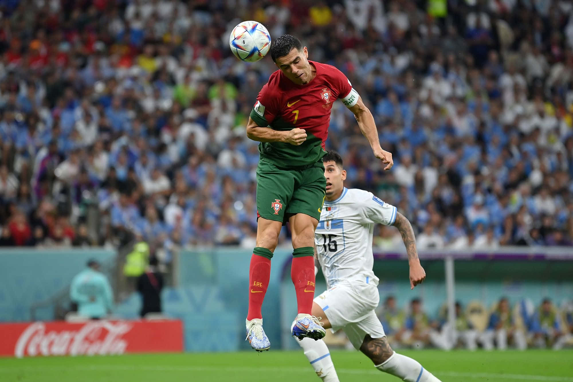 Cristiano Ronaldo 桌布 壁紙 — 一名身穿紅色球衣的足球員跳起頂球，而一名身穿白色球衣的後衛在下方爭搶，球場座無虛席。