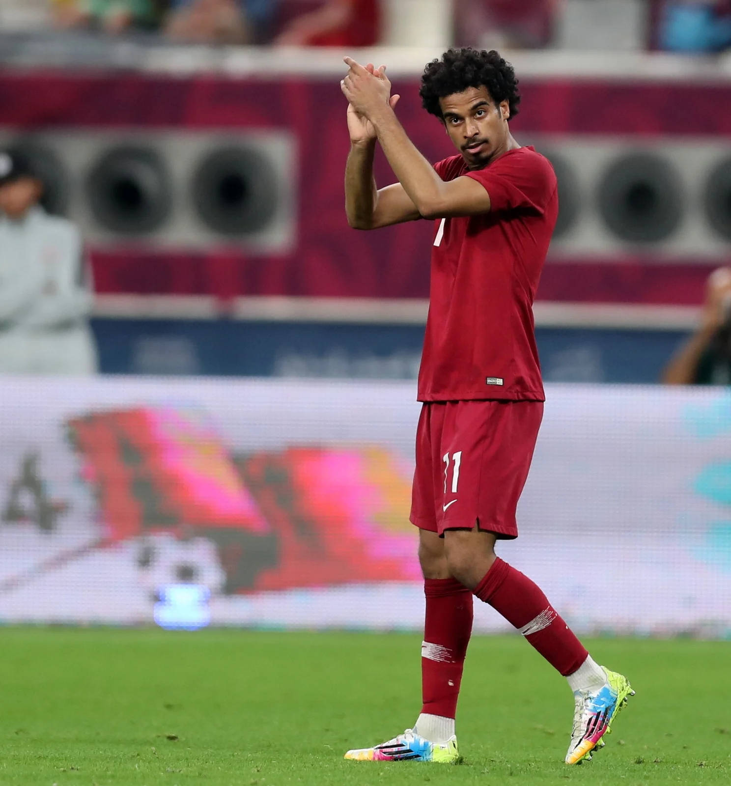 Qatar 桌布 壁紙 — 一名身穿紅色球衣的足球運動員在體育場燈光下，於充滿活力的綠色球場上拍手。