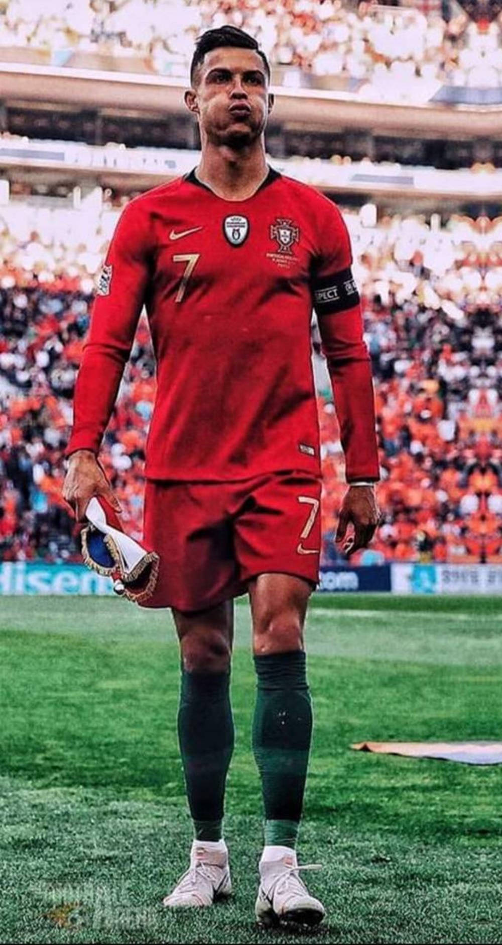 Cristiano Ronaldo 桌布 壁紙 — 一名身穿紅色葡萄牙球衣、號碼7的足球員在球場燈光下，莊嚴地走在綠色草地上，手裡拿著他的球靴。