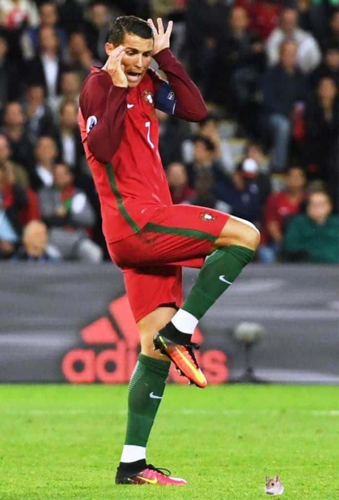 Ronaldo 桌布 壁紙 — 一名身穿紅色葡萄牙球衣的足球員在球場上雙手掩面並抬起一條腿慶祝。
