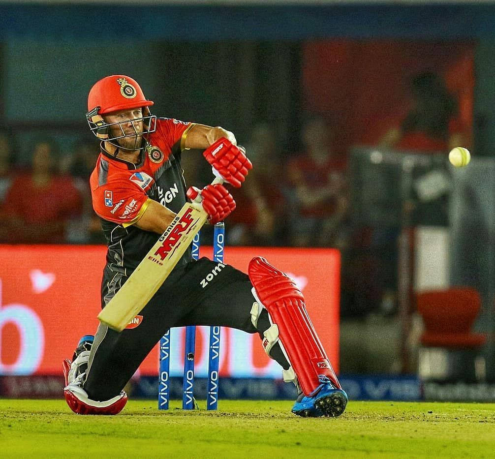AB De Villiers RCB IPL 2020 壁紙 — 一名身穿紅色裝備的板球擊球手在夜間比賽中，在體育場燈光下揮動球棒擊球。