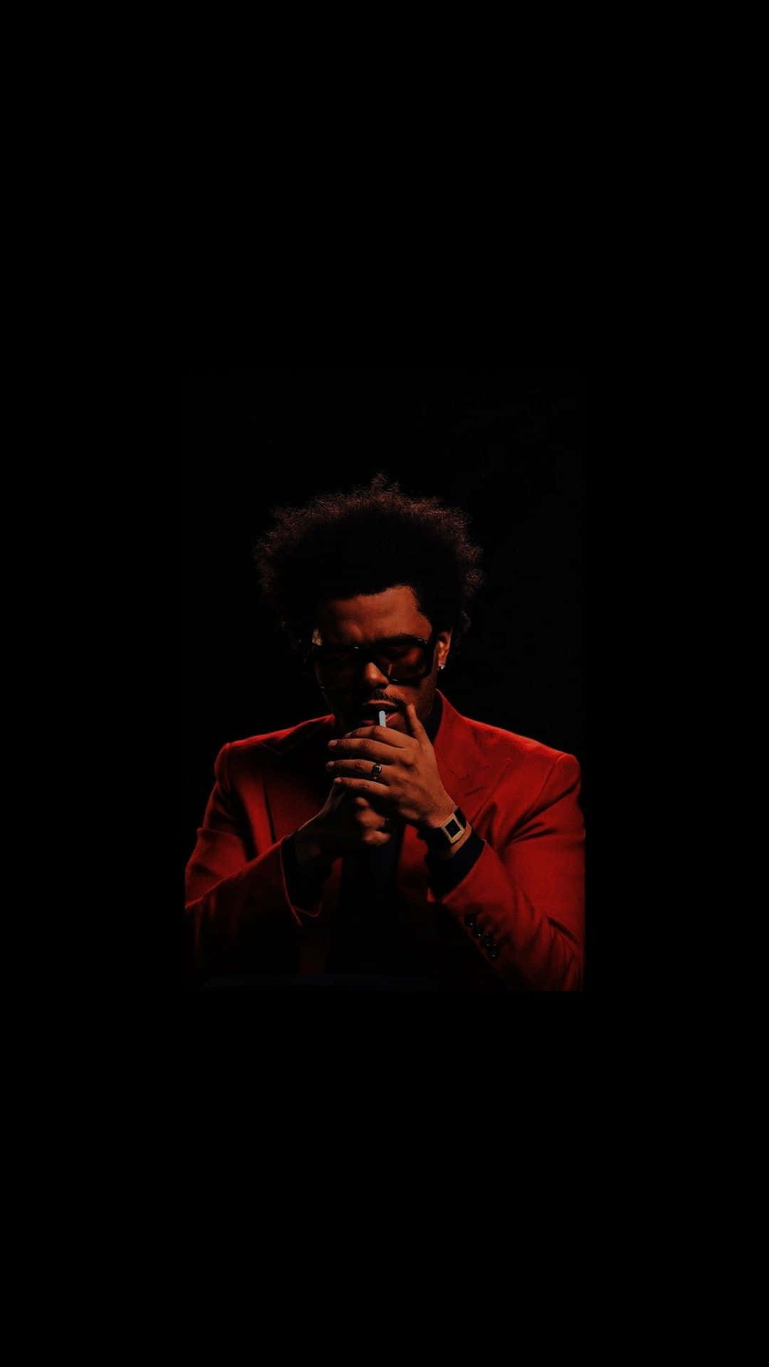 The Weeknd After Hours 桌布 壁紙 — 一名身穿紅色西裝、戴眼鏡的男子，在漆黑背景與戲劇性燈光下手持香煙。