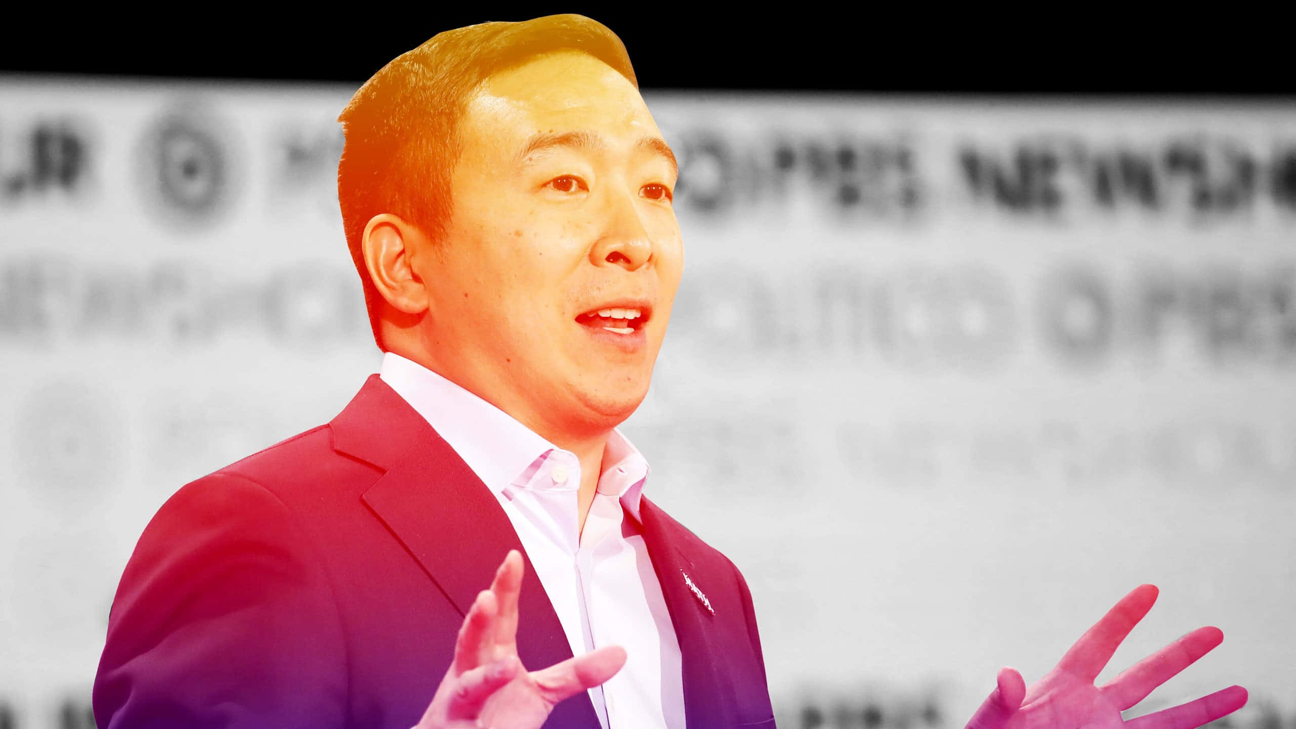 政治 桌布 壁紙 — 一名身穿紅色西裝的男子在會議上熱情地做手勢演講，背後有模糊的品牌標誌。