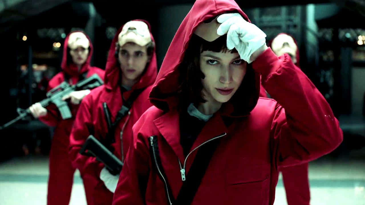 Money Heist 桌布 壁紙 — 一名身穿紅色連帽連身衣和白色手套的女子正在調整她的帽子，而其他穿著類似服裝的人在她身後手持武器。