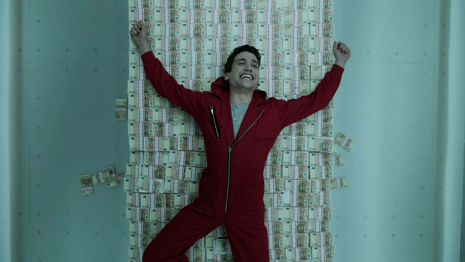 Money Heist 桌布 壁紙 — 一名身穿紅色連身衣的男子，對著堆滿歐元鈔票的牆壁，高舉雙臂，得意地大笑。