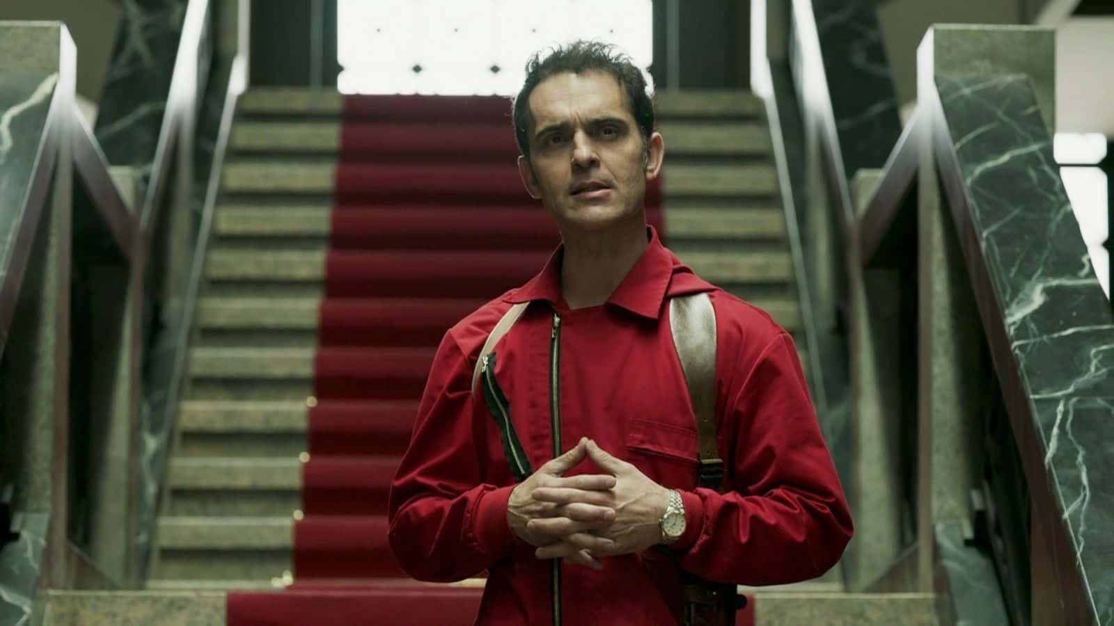 Money Heist 桌布 壁紙 — 一名身穿紅色連身衣的男子站在鋪有紅地毯和大理石欄杆的大樓梯底部。