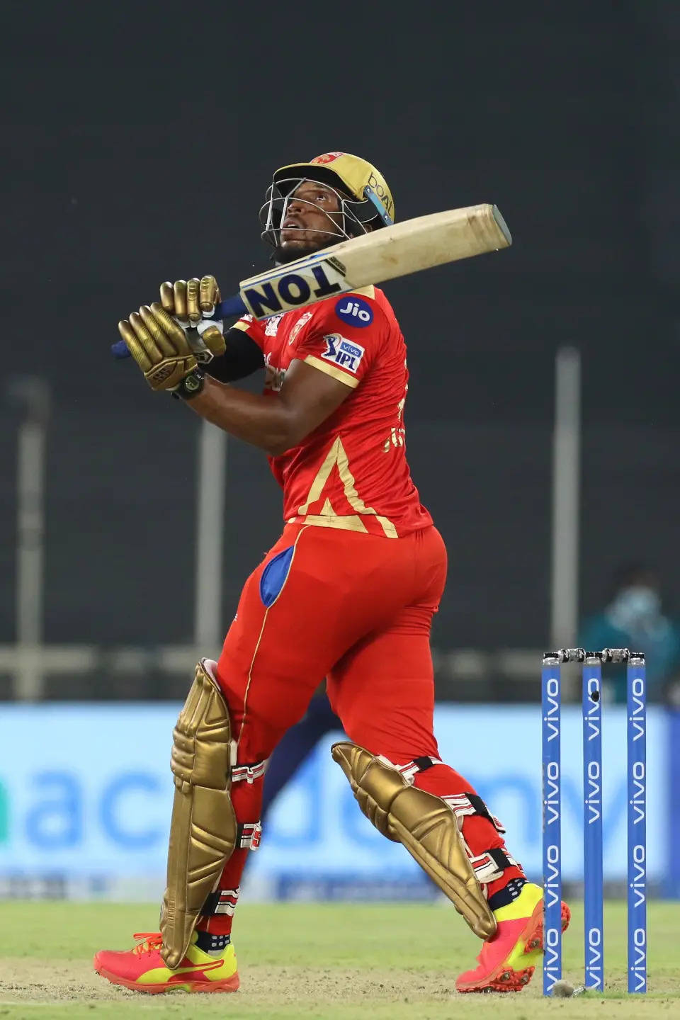 Ipl 2021 桌布 壁紙 — 一名身穿紅金裝備的板球擊球手在夜間比賽中，於球場燈光下強力揮棒。