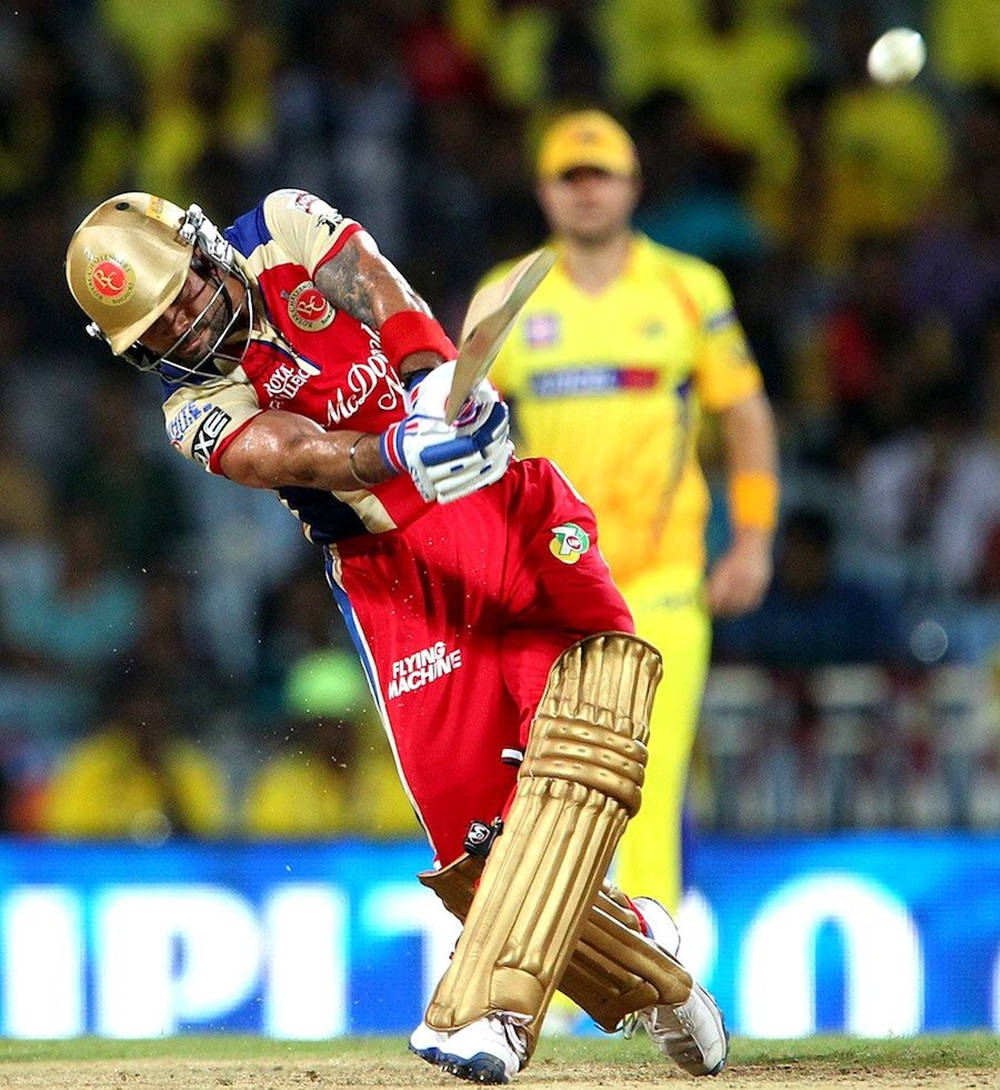 royal challengers bangalore 桌布 壁紙 — 一名身穿紅金裝備的板球擊球手在夜間比賽中，於球場燈光下強力揮棒擊球。