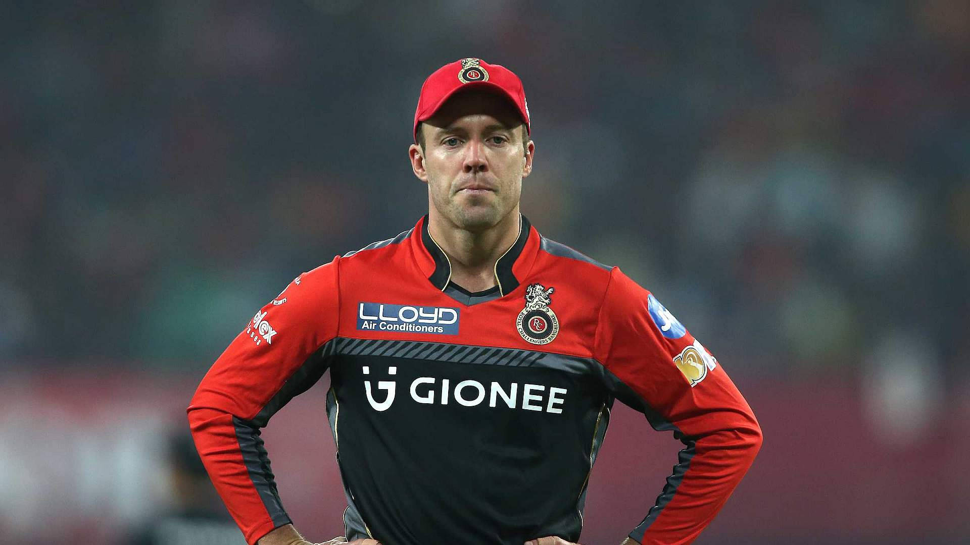 royal challengers bangalore 桌布 壁紙 — 一名身穿紅黑色球衣的板球運動員在球場燈光下比賽時，雙手叉腰，神情專注地站立。