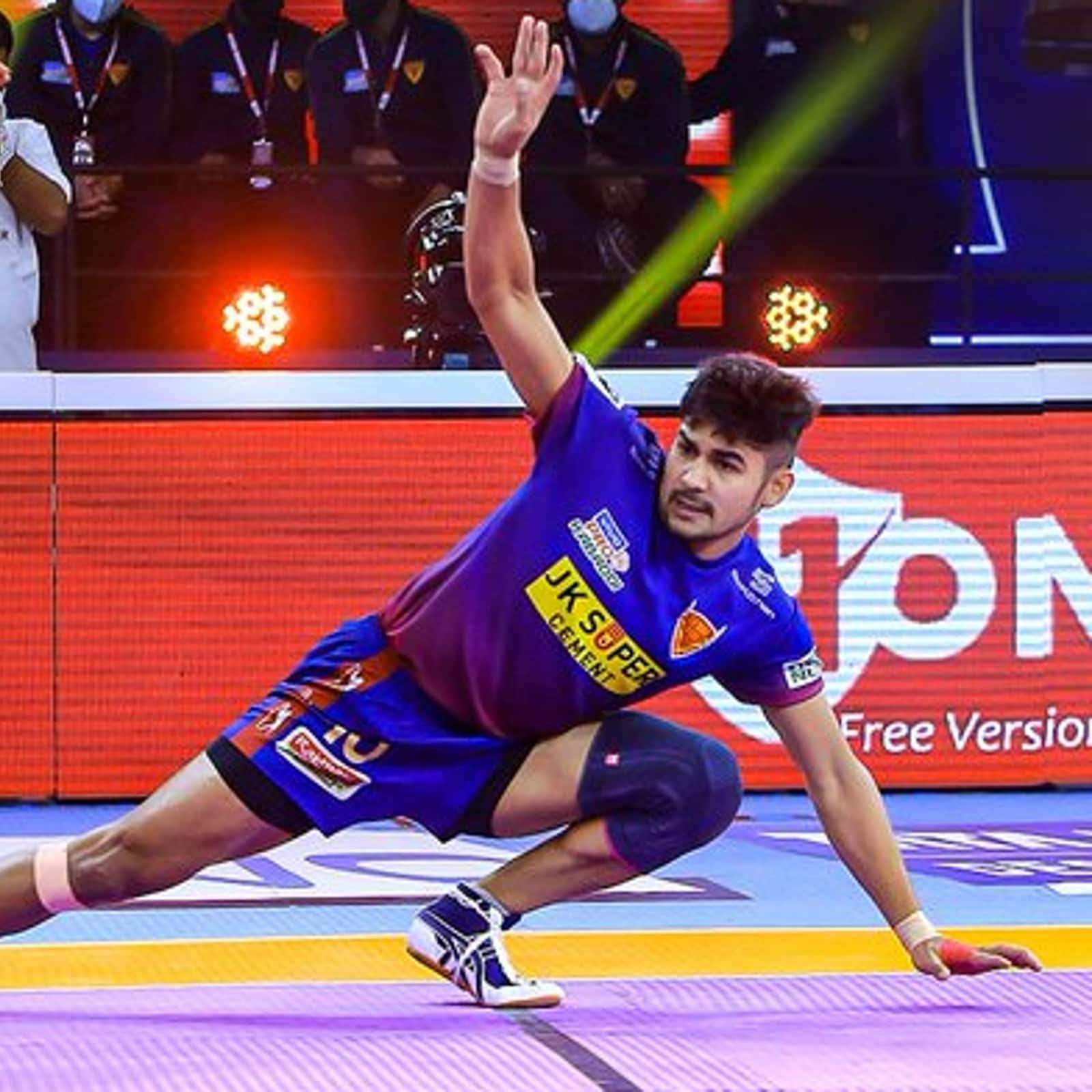Kabaddi 桌布 壁紙 — 一名身穿紫色球衣的手球運動員在明亮的場館燈光下，在充滿活力的球場上低身撲出。