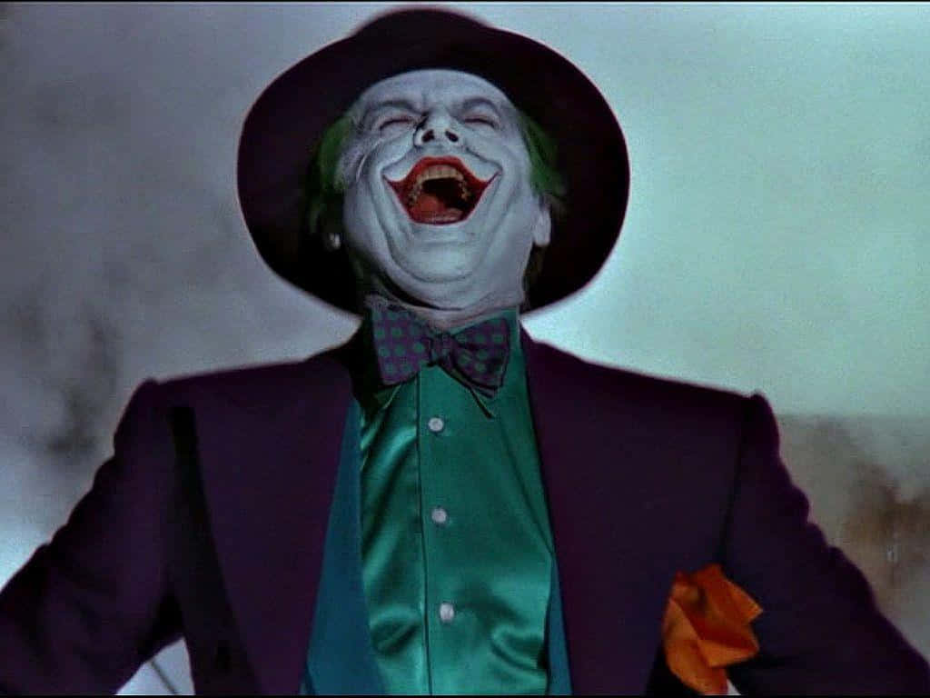 Joker Laughing 桌布 壁紙 — 一名身穿紫色西裝和綠色襯衫的男子，臉上塗著白色顏料、紅唇、綠髮，戴著黑色帽子，狂笑不止。