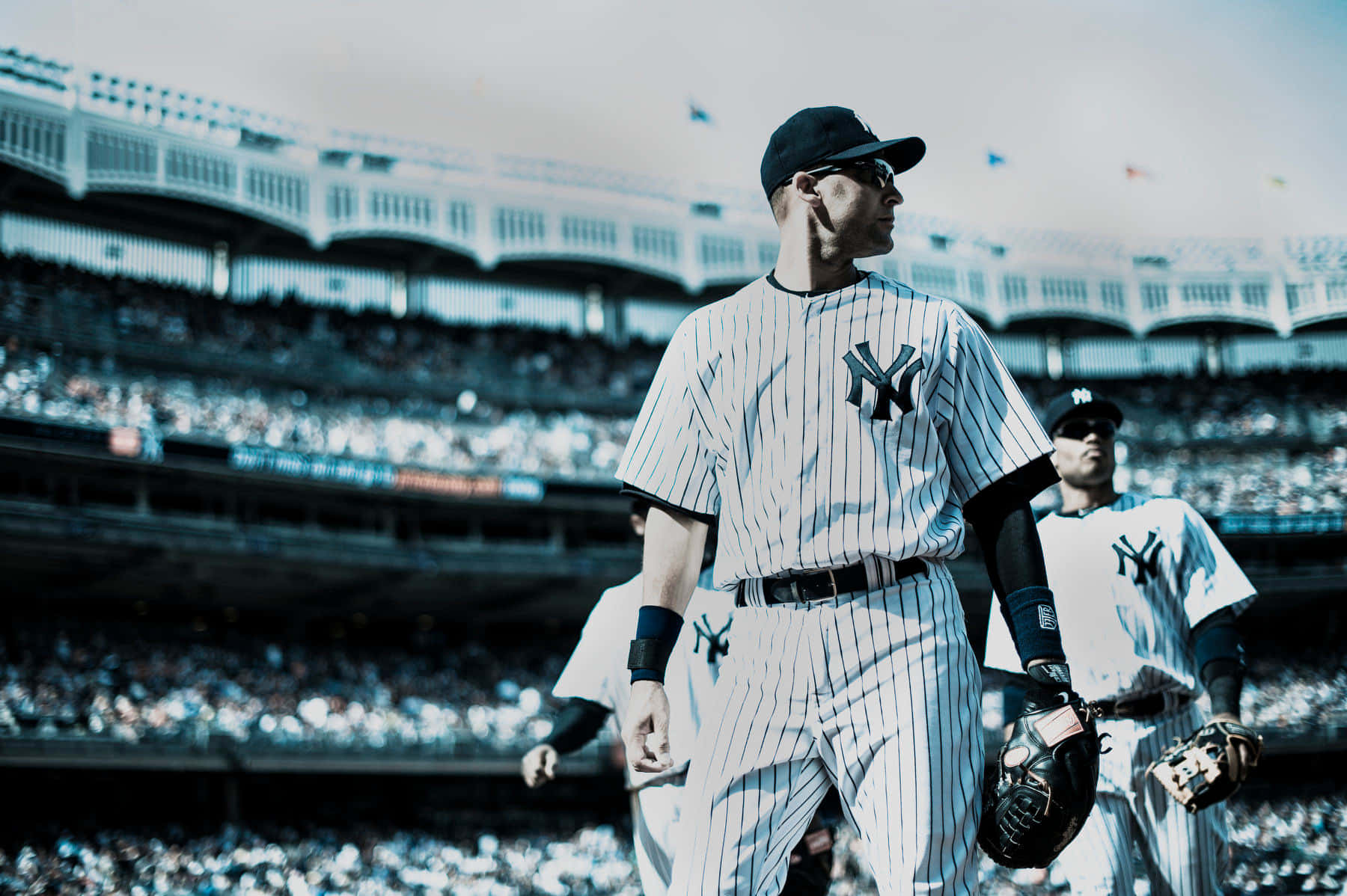 Baseball Cards 桌布 壁紙 — 一名身穿細條紋球衣的紐約洋基棒球運動員在明亮的日光下自信地走過擠滿觀眾的球場。