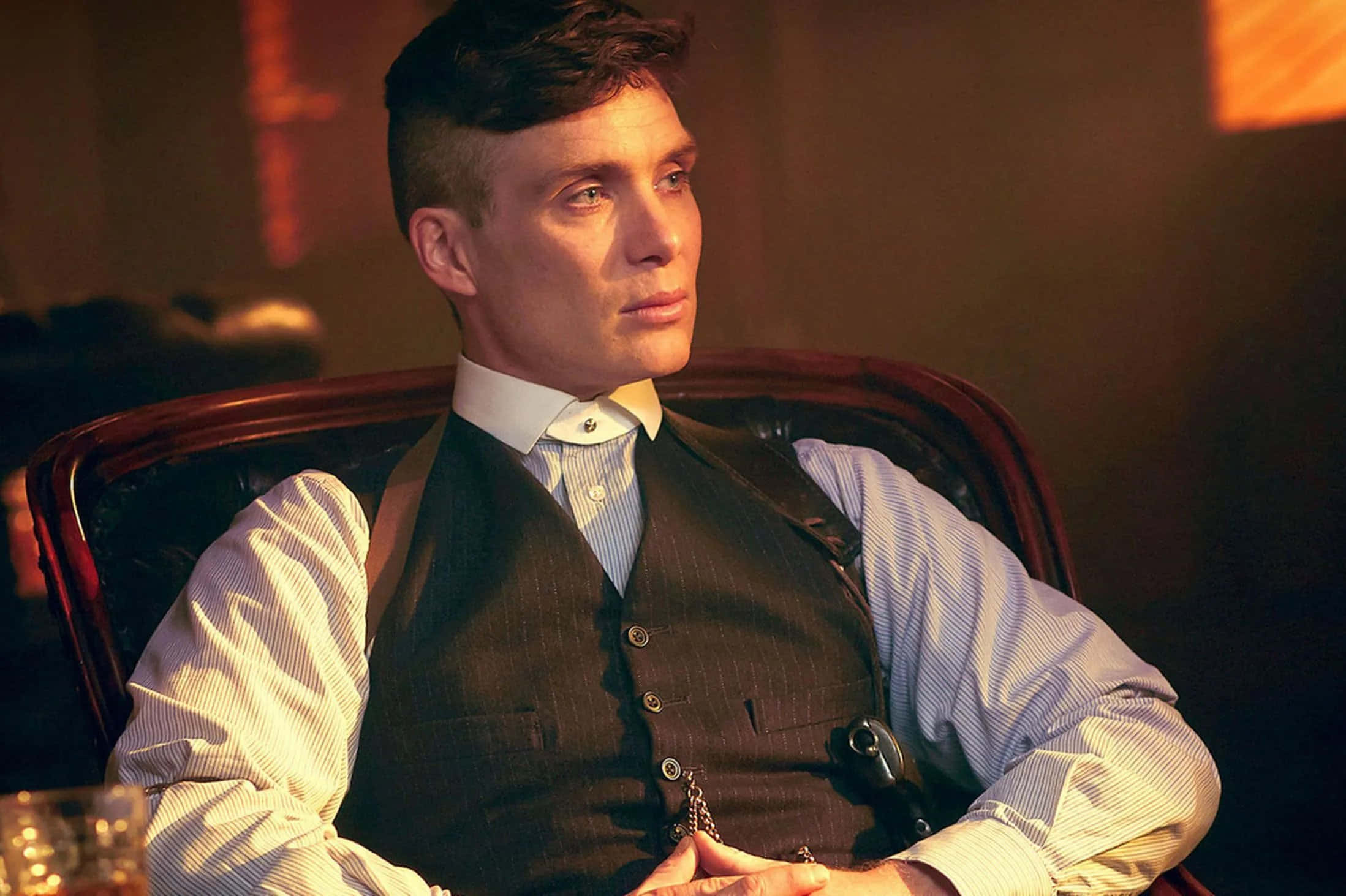 Peaky Blinders 桌布 壁紙 — 一名身穿細條紋背心的男士坐在皮革椅上，溫暖的琥珀色燈光下，旁邊放著一杯威士忌。