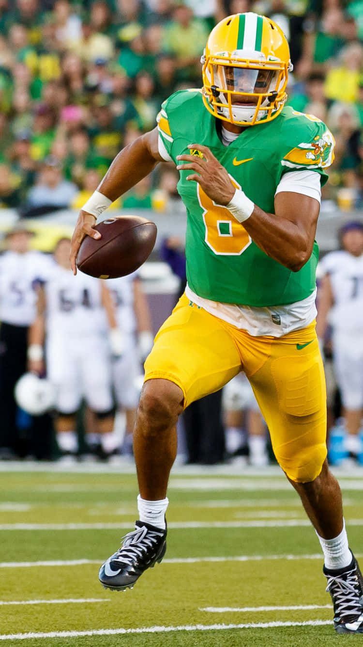 Oregon Ducks 桌布 壁紙 — 一名身穿綠色和黃色球衣的美式足球四分衛在草地上擲球，背景有模糊的觀眾。