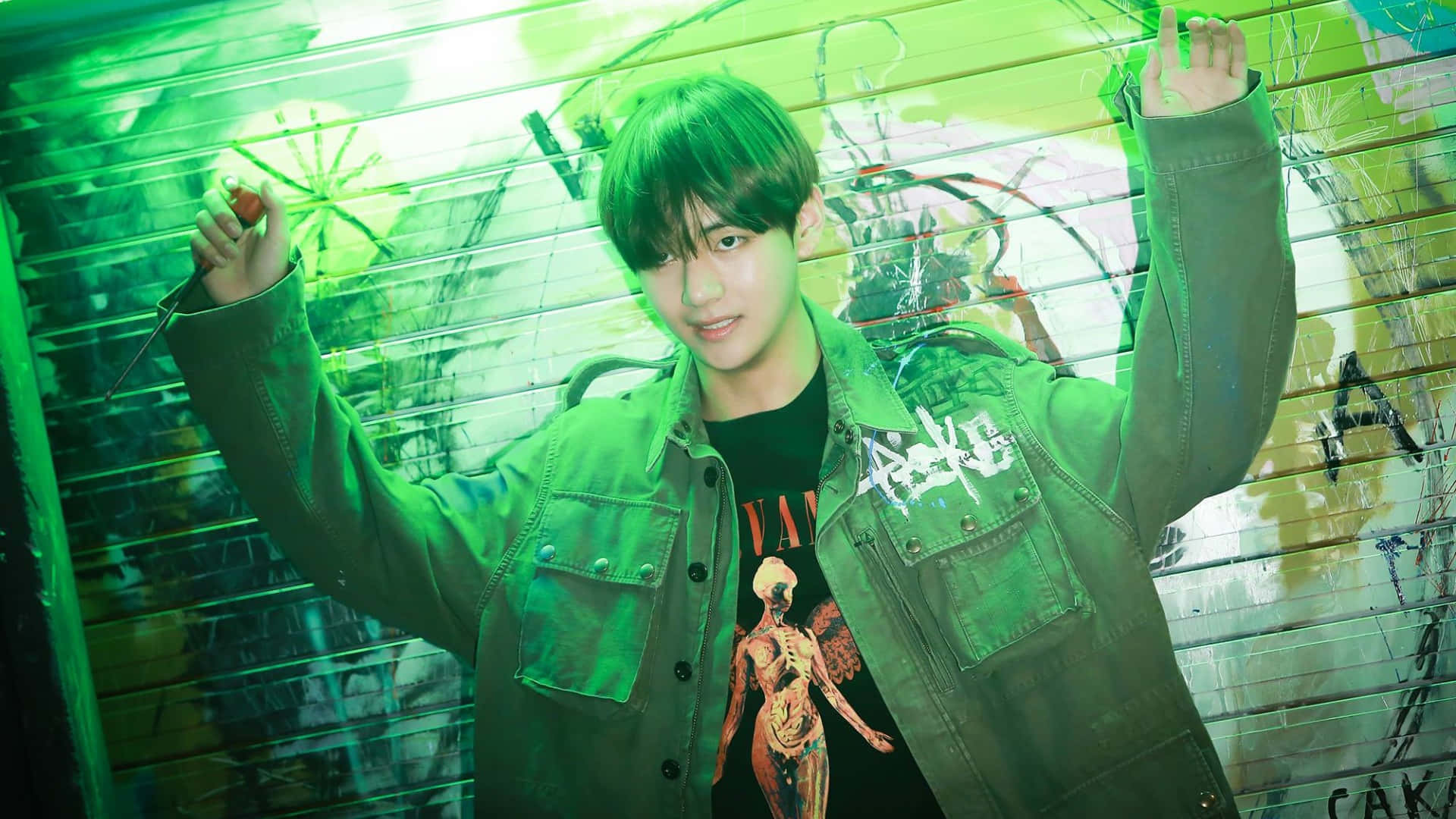 Taehyung Cute 桌布 壁紙 — 一名身穿綠色外套和圖案T恤的年輕男子，在霓虹綠光照耀的塗鴉牆前自信地擺姿勢。