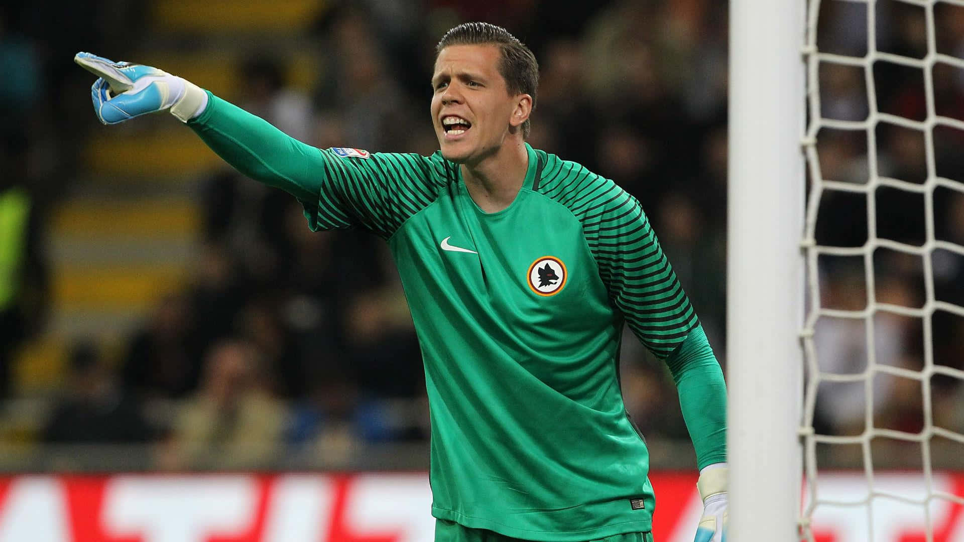 Wojciech Szczesny 桌布 壁紙 — 一名身穿綠色條紋球衣的足球守門員在比賽期間在球門柱附近大聲喊叫並用力做手勢。