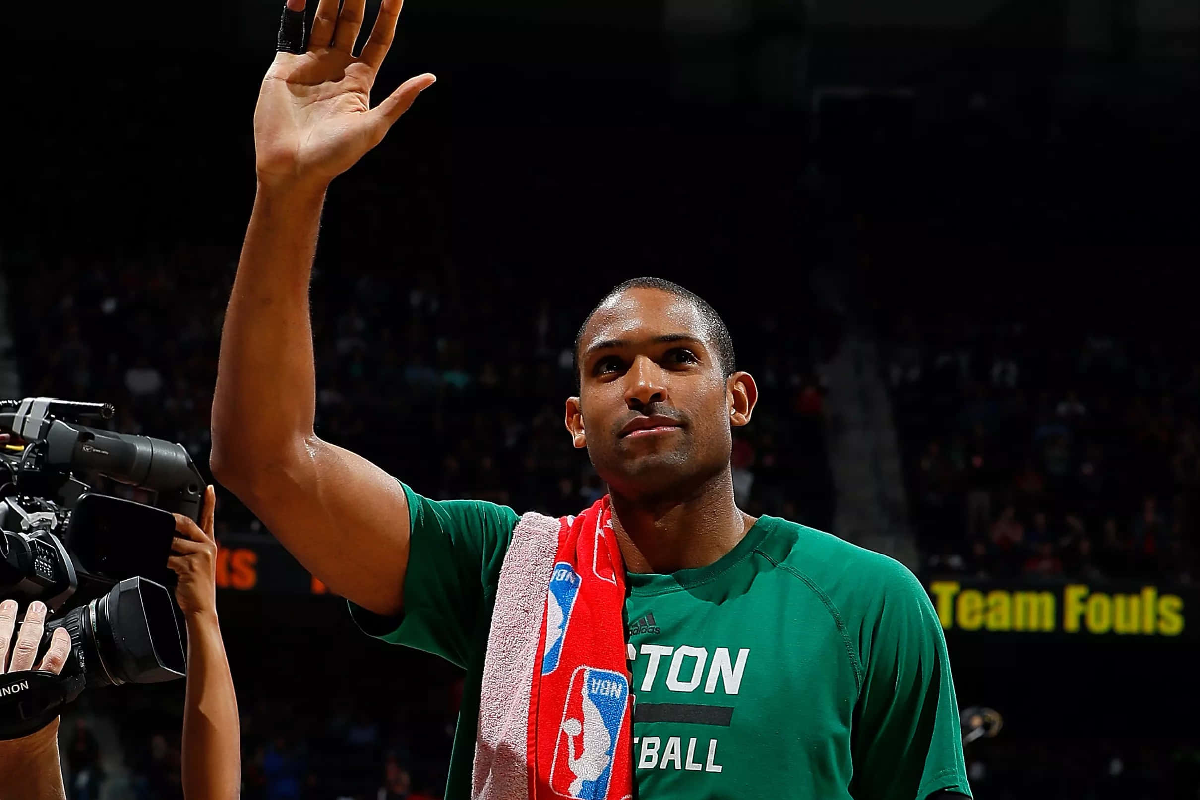 Al Horford 桌布 壁紙 — 一名身穿綠色波士頓塞爾特人球衣的籃球運動員，在比賽中將紅色毛巾搭在肩上，向球迷揮手。