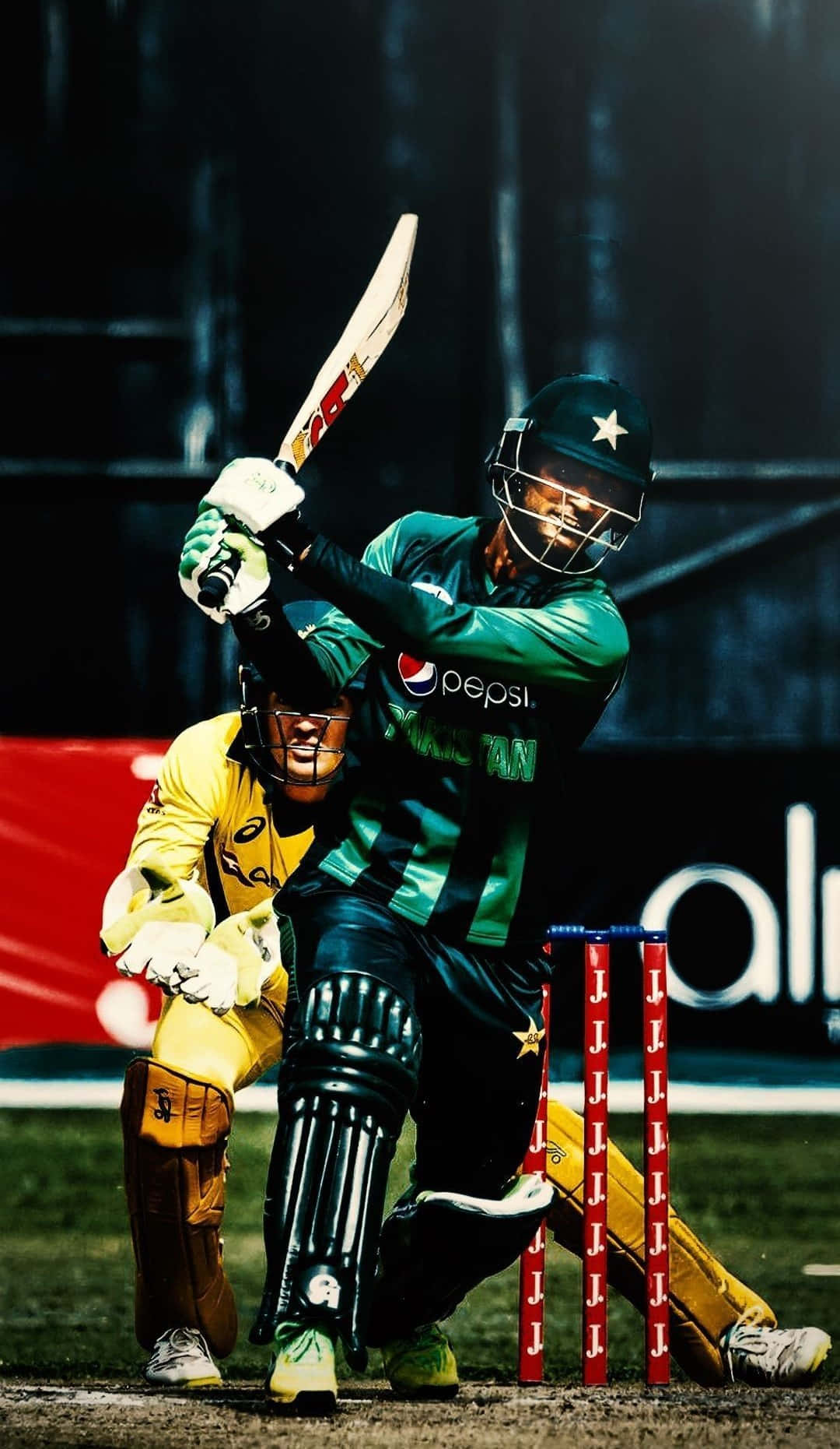 Cricket 桌布 壁紙 — 一名身穿綠色球衣的板球擊球手強力揮棒擊球，身後有一名身穿黃色球衣的守門員蹲伏著。