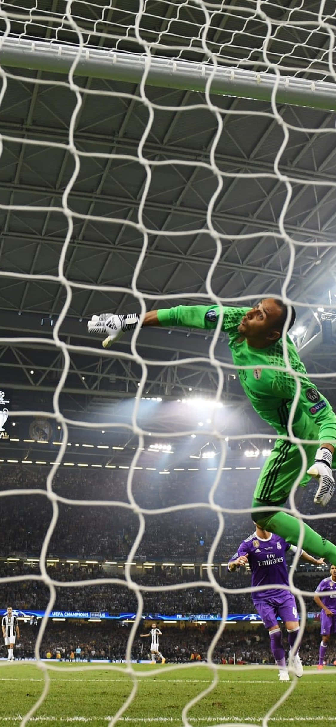 Keylor Navas 桌布 壁紙 — 一名身穿綠色球衣的足球守門員在夜間比賽中跳過球網，在球場燈光下阻擋射門。