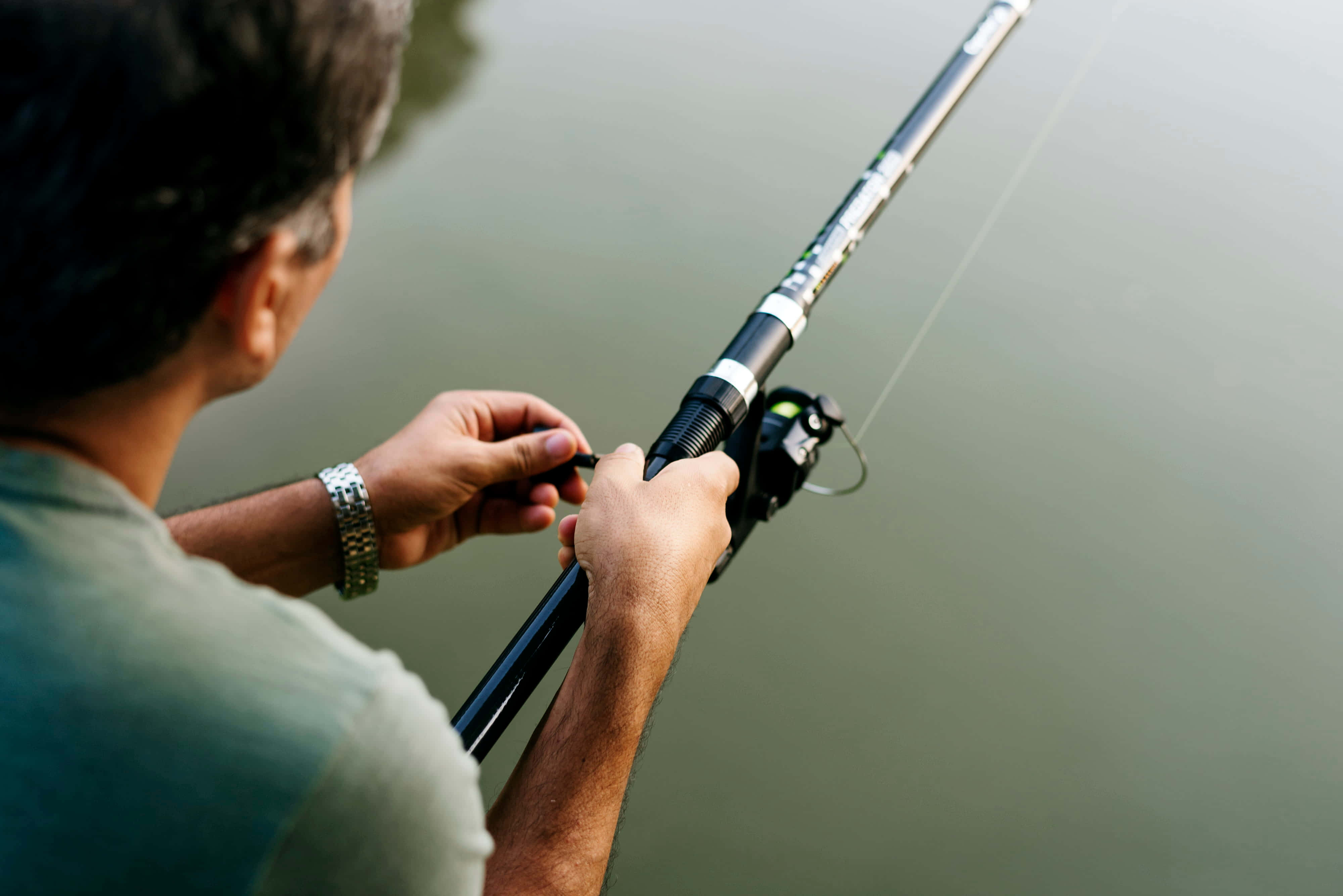 Fishing Bait 桌布 壁紙 — 一名身穿綠色襯衫的男子在寧靜的湖邊將魚竿拋入平靜的水中。