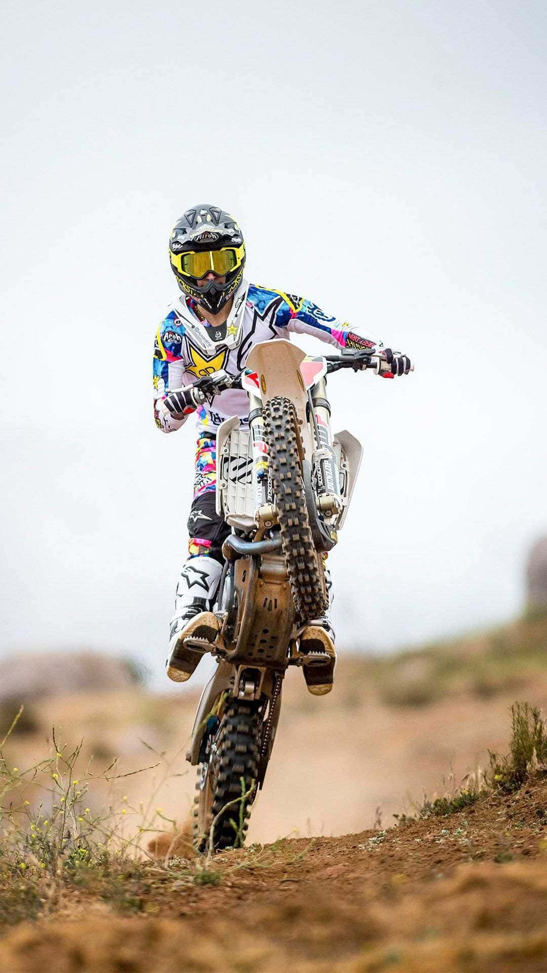 Dirtbike 桌布 壁紙 — 一名身穿色彩繽紛裝備的越野電單車手，在多雲天空下嘅塵土小徑上傾斜入彎。