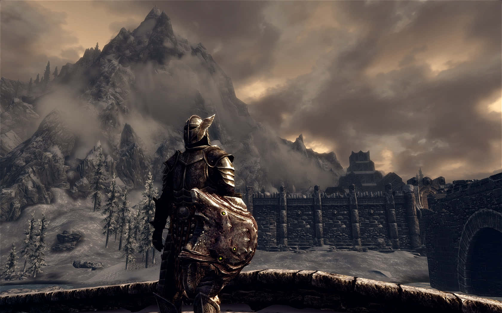 Skyrim Windhelm 桌布 壁紙 — 一名身穿華麗盔甲的騎士站在石橋上，俯瞰著風暴天空下白雪覆蓋的要塞和崎嶇的山脈。