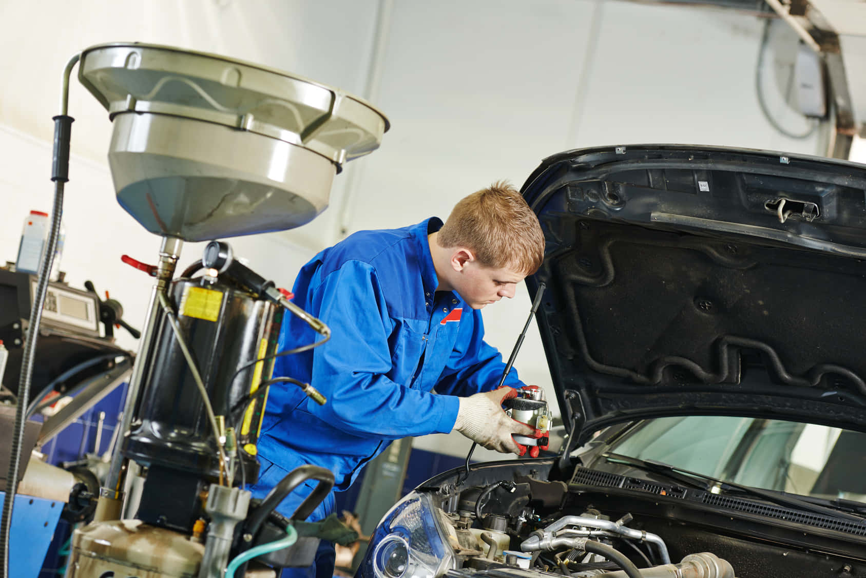 Car Repair 桌布 壁紙 — 一名身穿藍色制服的機械師在明亮的車間燈光下小心地更換汽車引擎零件。