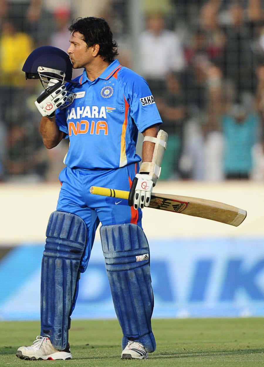 Sachin Tendulkar 桌布 壁紙 — 一名身穿藍色印度隊服的板球運動員在夜間球場燈光下，站在綠色場地上，將頭盔貼近臉部並手持球棒。