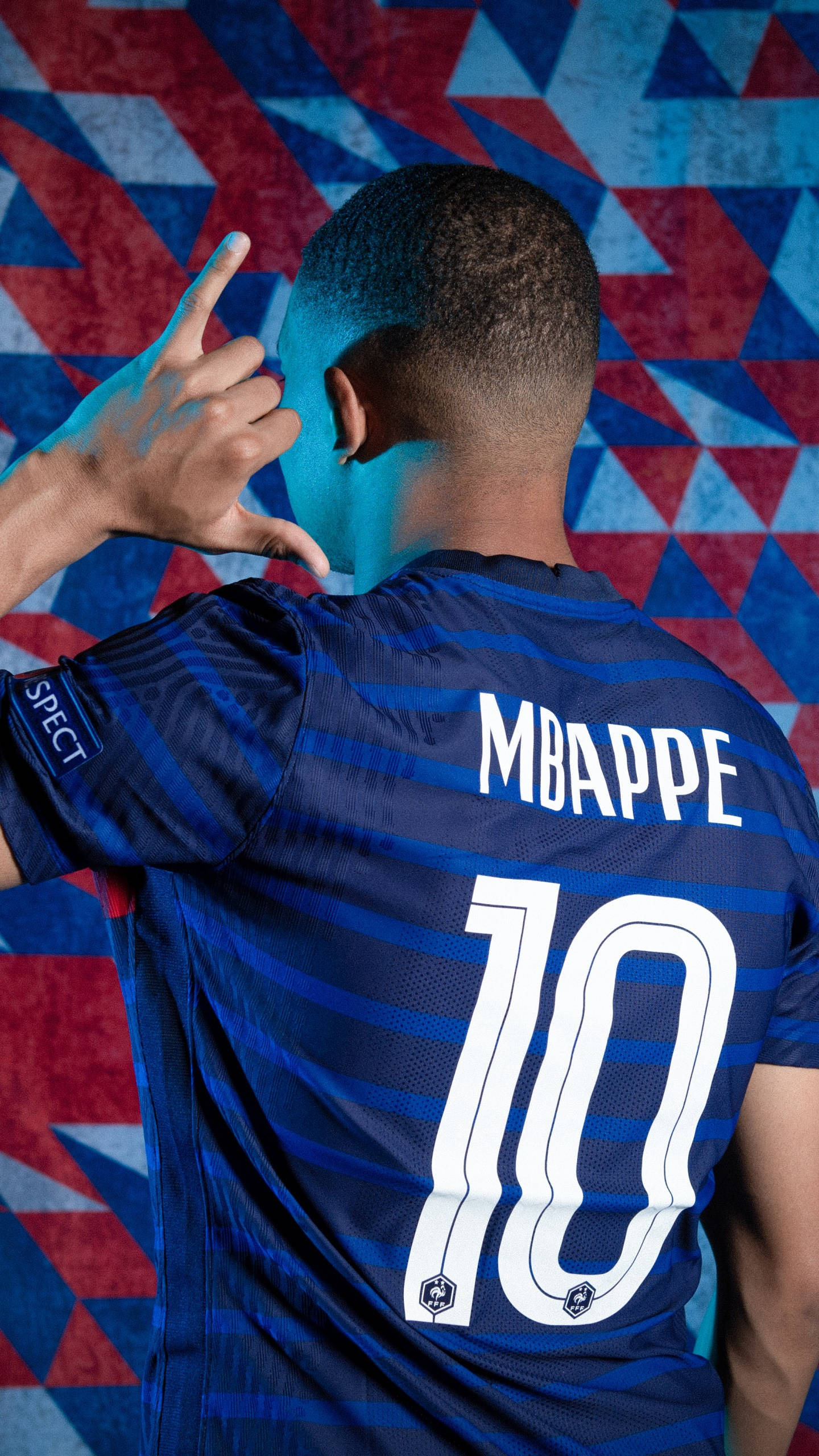 Football Players 桌布 壁紙 — 一名身穿藍色條紋球衣、背後印有「MBAPPE」和「10」的足球員，在幾何紅藍背景下做出手勢。