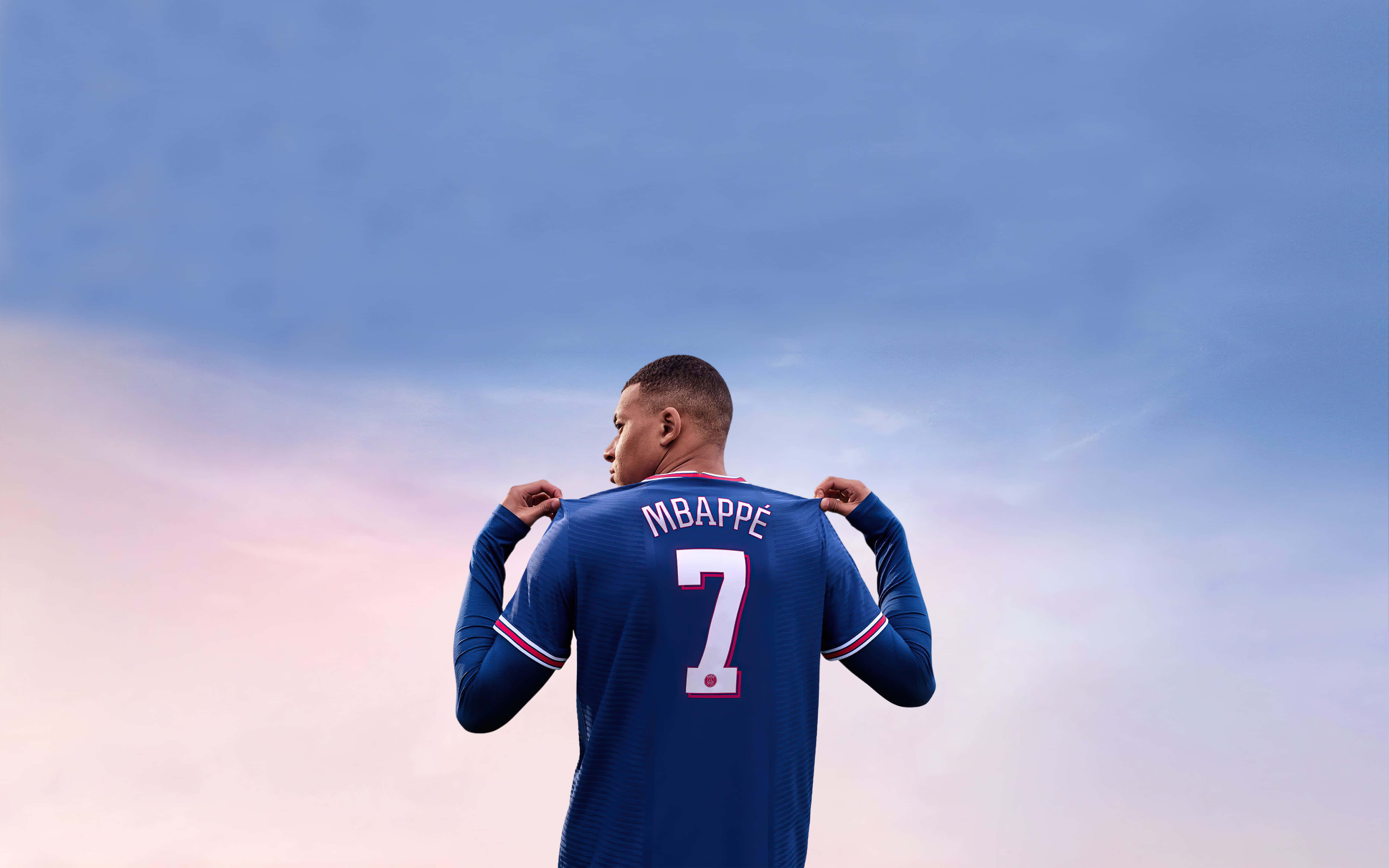 Mbappe 桌布 壁紙 — 一名身穿藍色球衣、背號7號、名字為Mbappé的足球員背對鏡頭，背景是柔和的粉紅色和藍色天空。