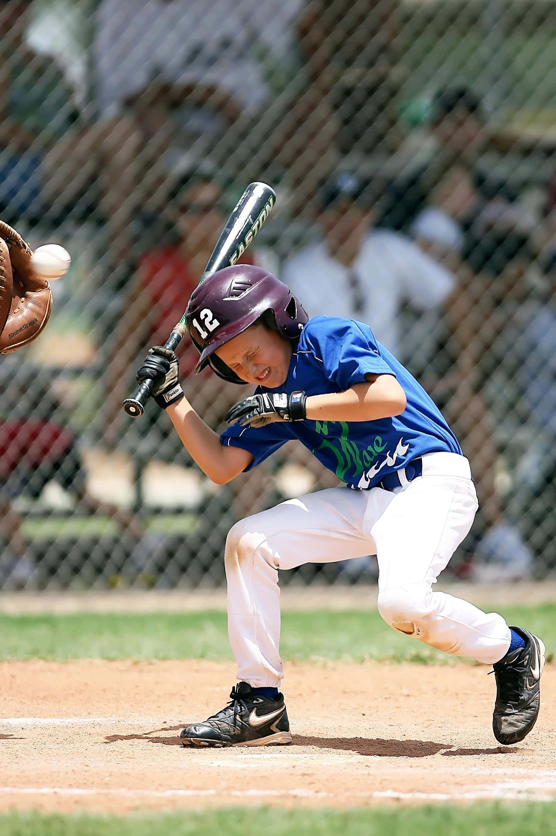 Little League Baseball 桌布 壁紙 — 一名身穿藍色球衣和紫色頭盔的年輕棒球手，在球接近時，專注地揮動球棒。