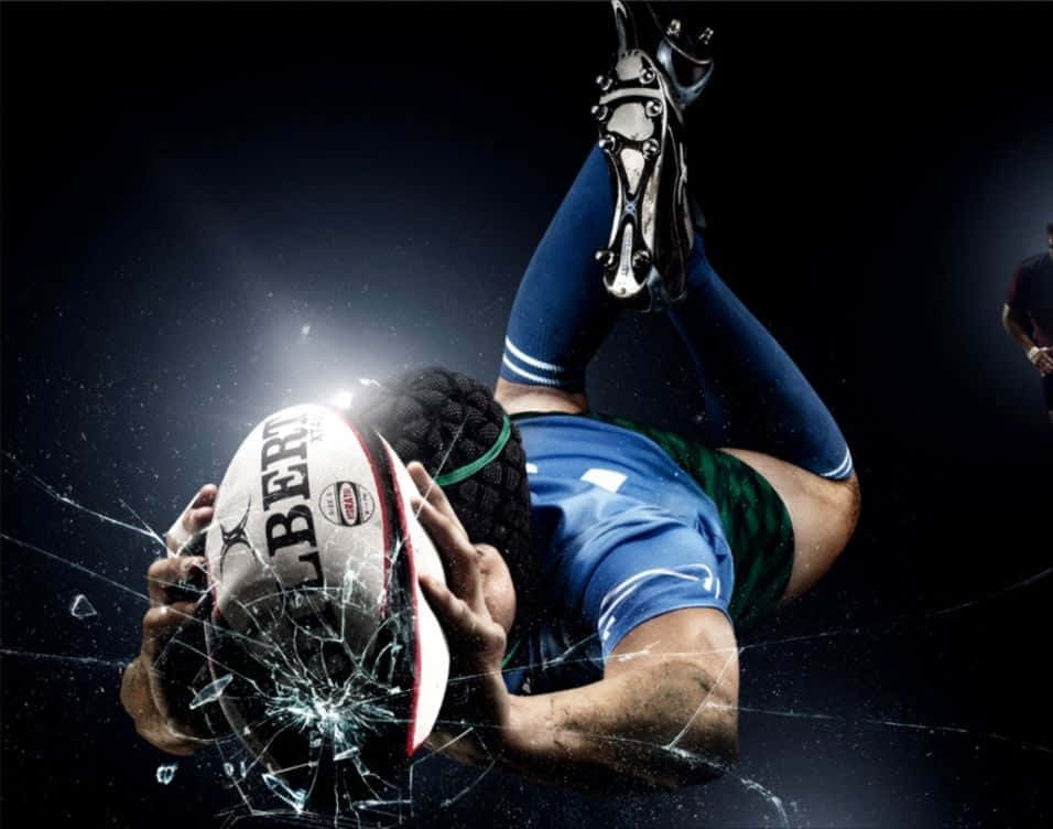 Rugby 桌布 壁紙 — 一名身穿藍色球衣的欖球運動員在黑暗背景下手持球衝破碎玻璃。