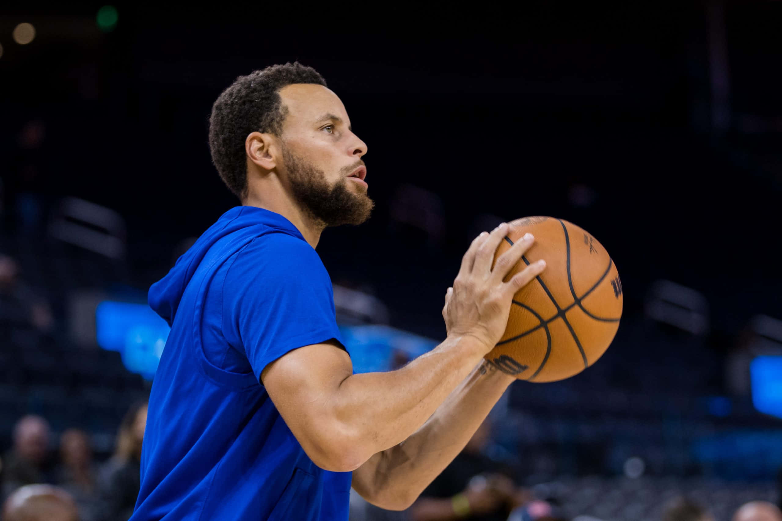 steph curry 桌布 壁紙 — 一名身穿藍色球衣的籃球運動員在場館燈光下準備投籃，背景有模糊的觀眾。