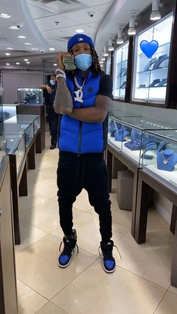 King Von 桌布 壁紙 — 一名身穿藍色背心和帽子的男子在設有玻璃陳列櫃的珠寶店內，戴著口罩手持現金。