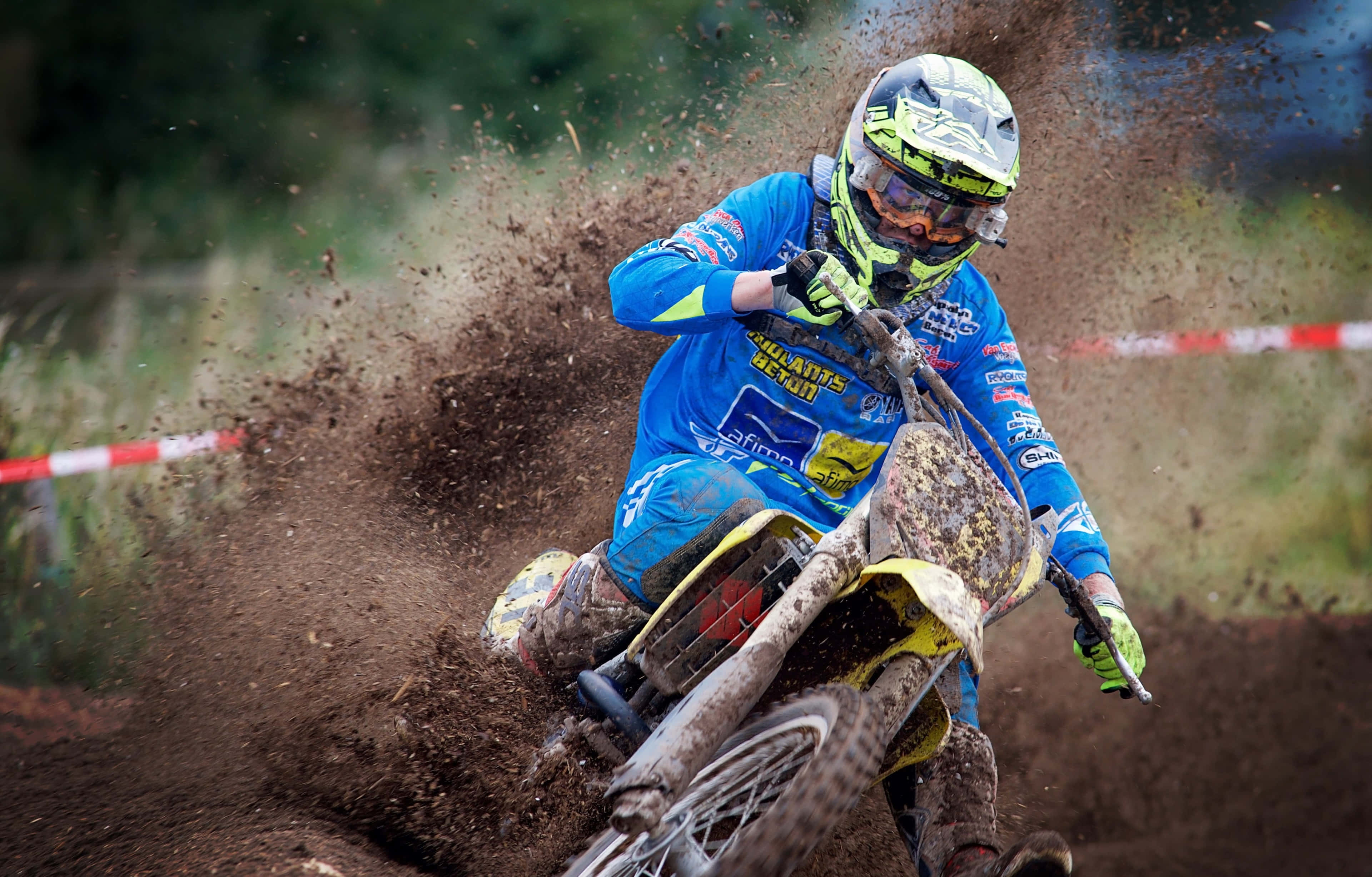 Motocross 桌布 壁紙 — 一名身穿藍色裝備的越野電單車手在森林賽道上傾斜入泥濘彎道，揚起泥土。