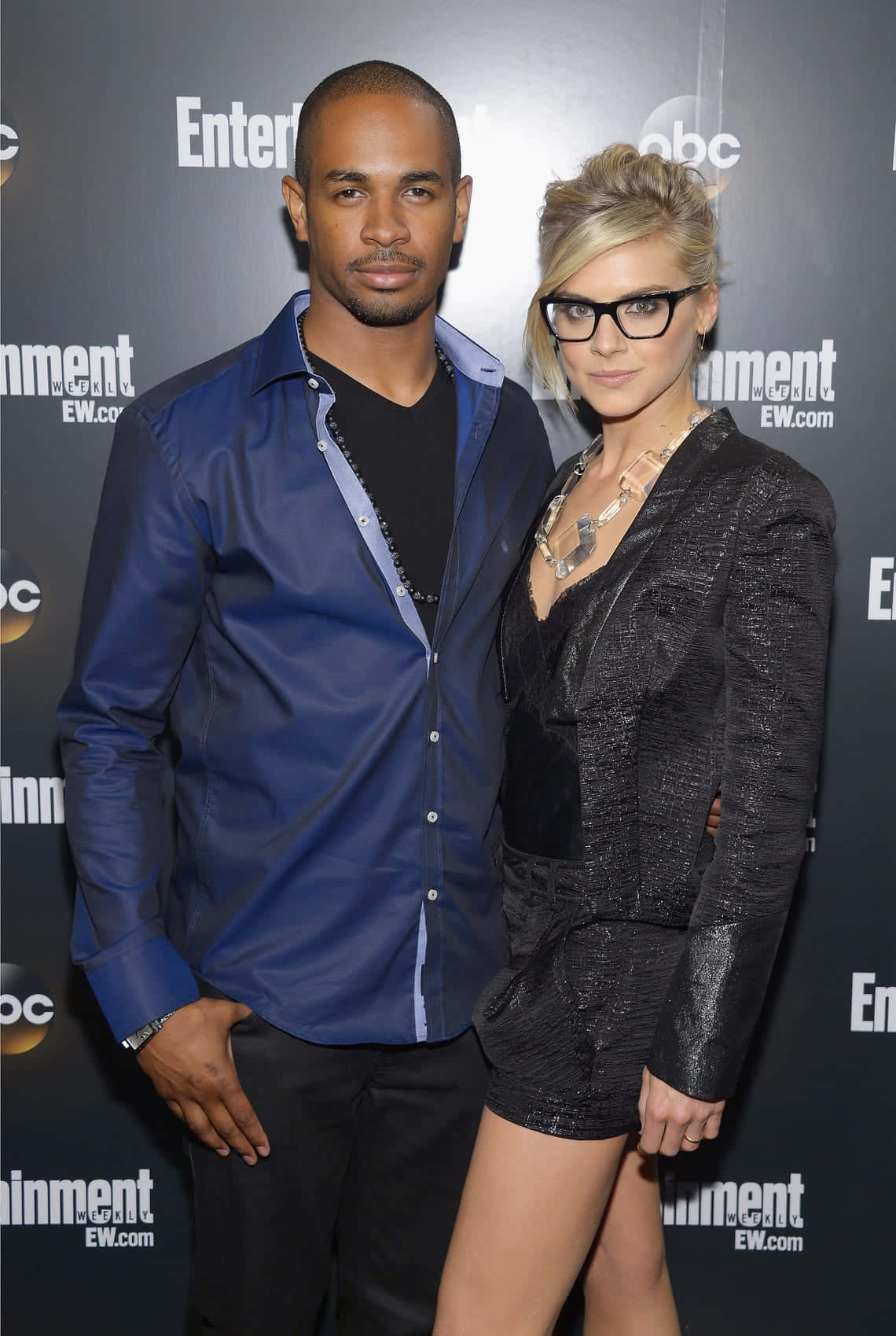 eliza coupe 桌布 壁紙 — 一名身穿藍色襯衫的男子和一名身穿黑色服裝的女子在一個 Entertainment Weekly 活動中一起擺姿勢，背後有標誌。